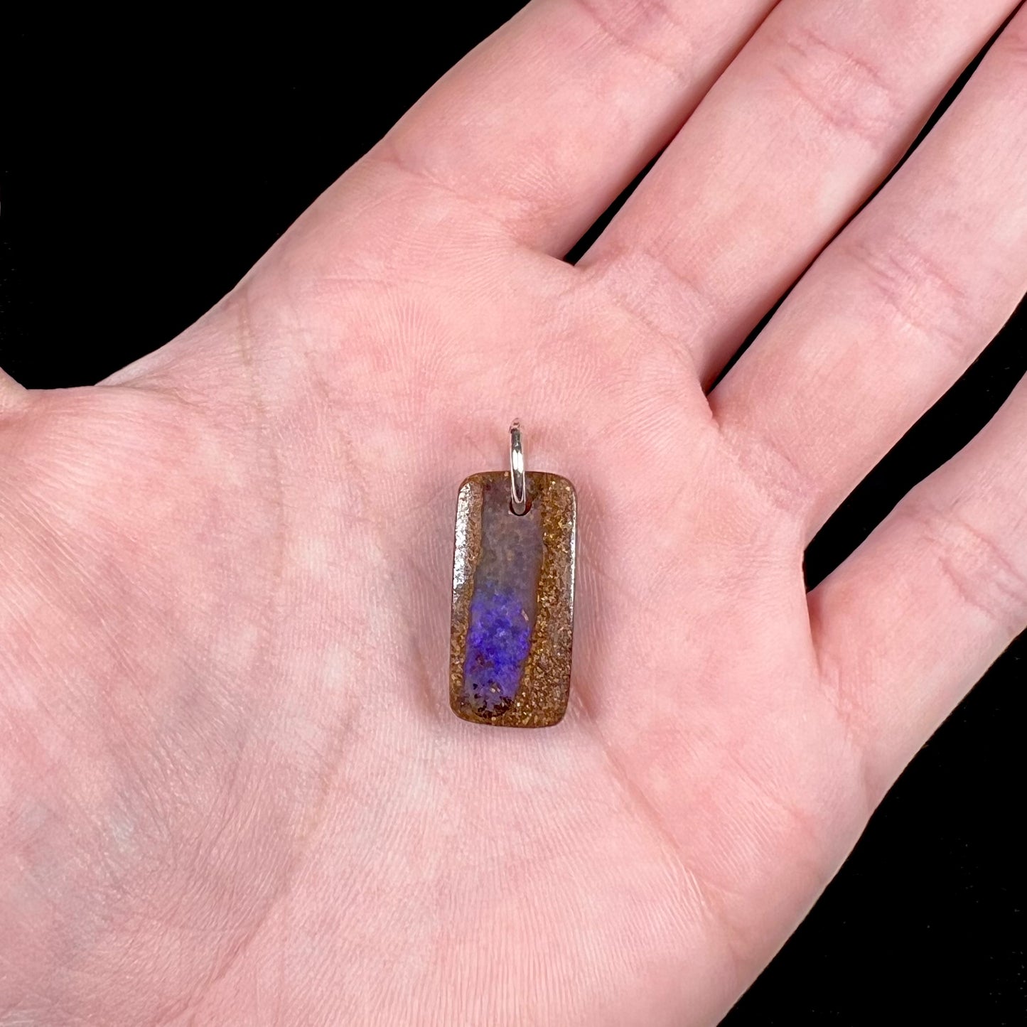 A drilled boulder opal stone with a sterling silver ring through the hole to be worn as a pendant.