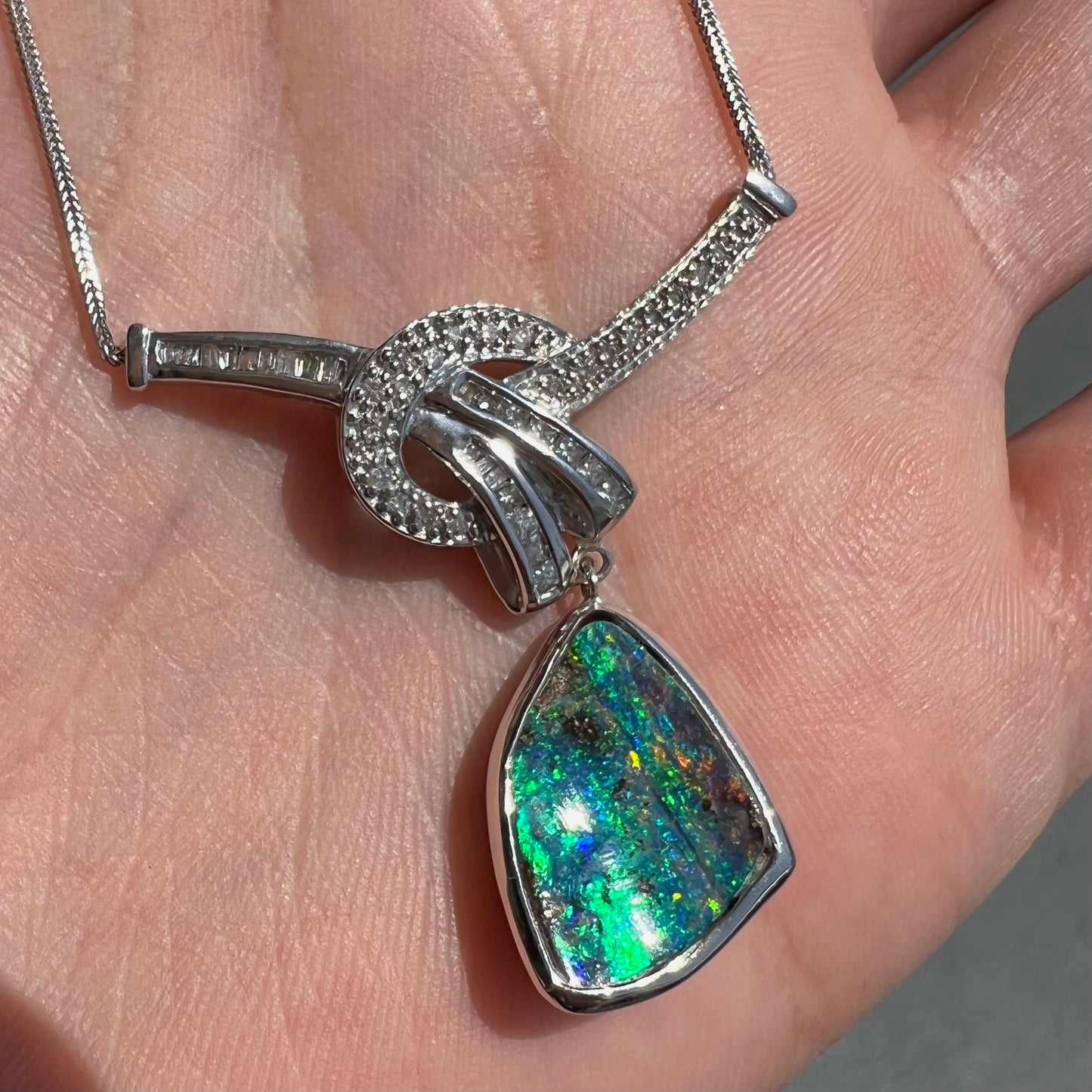 A white gold necklace set with diamonds and a dangling, bezel set boulder opal.