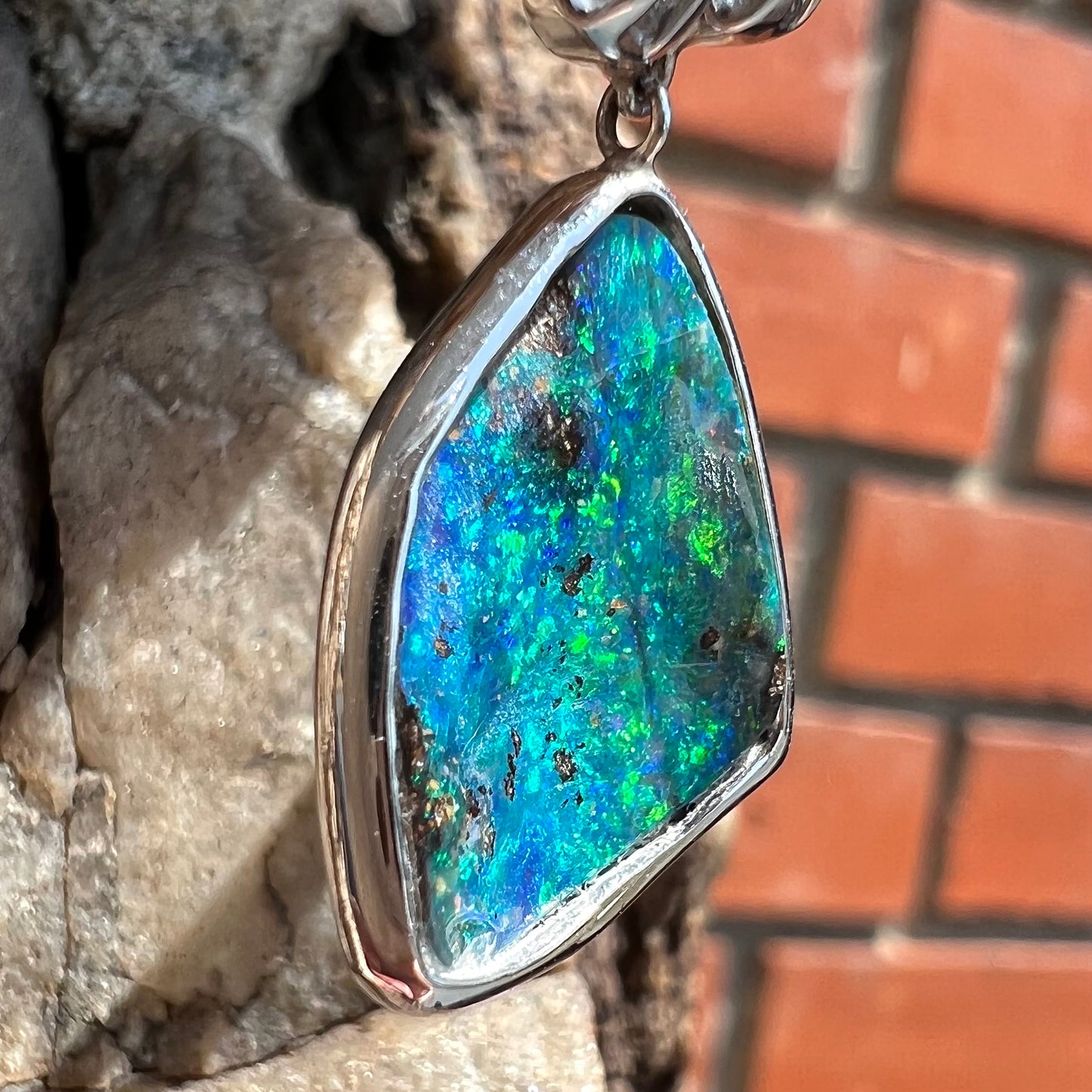 A white gold necklace set with diamonds and a dangling, bezel set boulder opal.