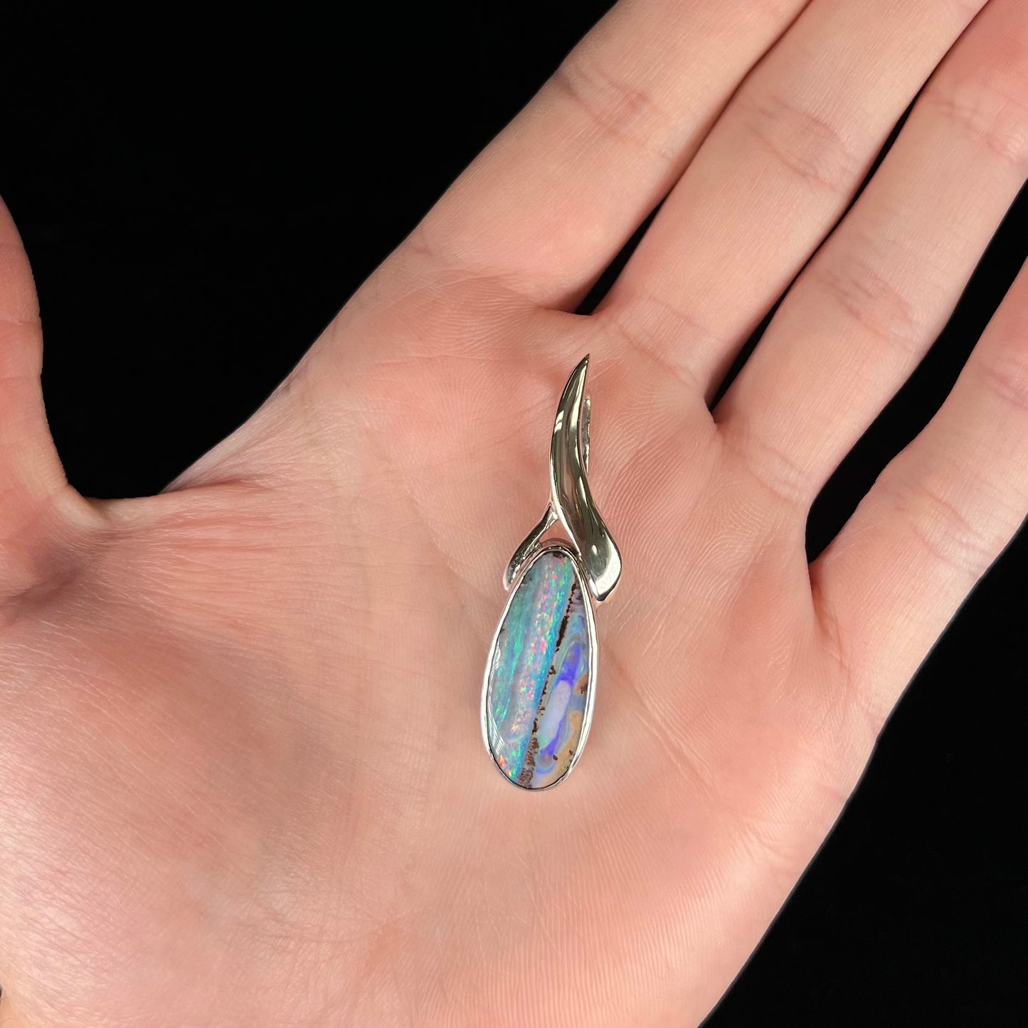 A white gold solitaire pendant set with an Quilpie, Australian boulder opal stone. The opal shines a rainbow of colors.