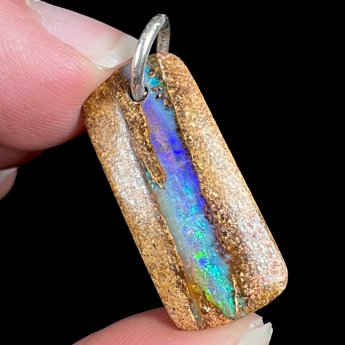 A drilled boulder opal stone with a sterling silver ring through the hole to be worn as a pendant.