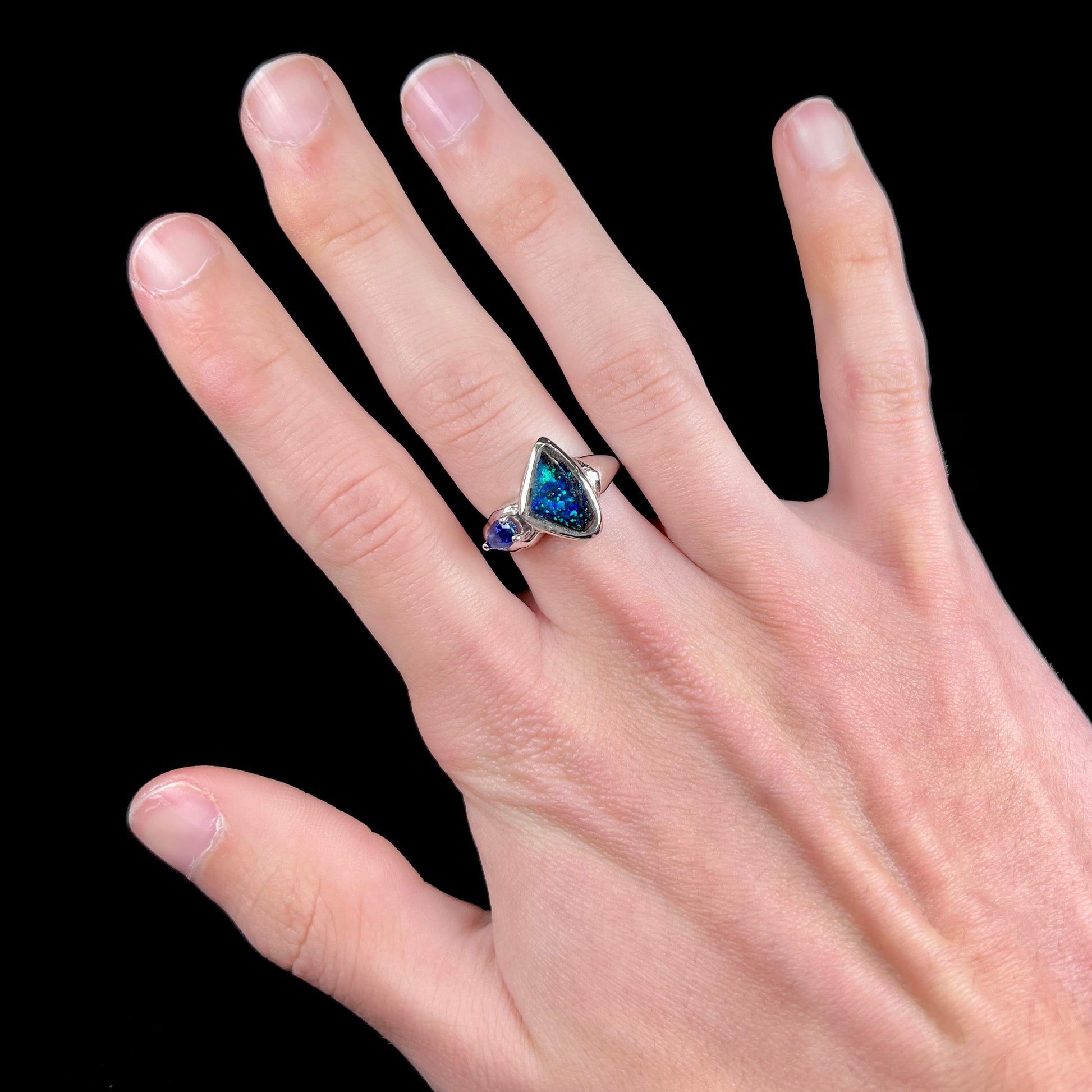A ladies' white gold ring set with Australian black boulder opal and pear shape blue sapphire.