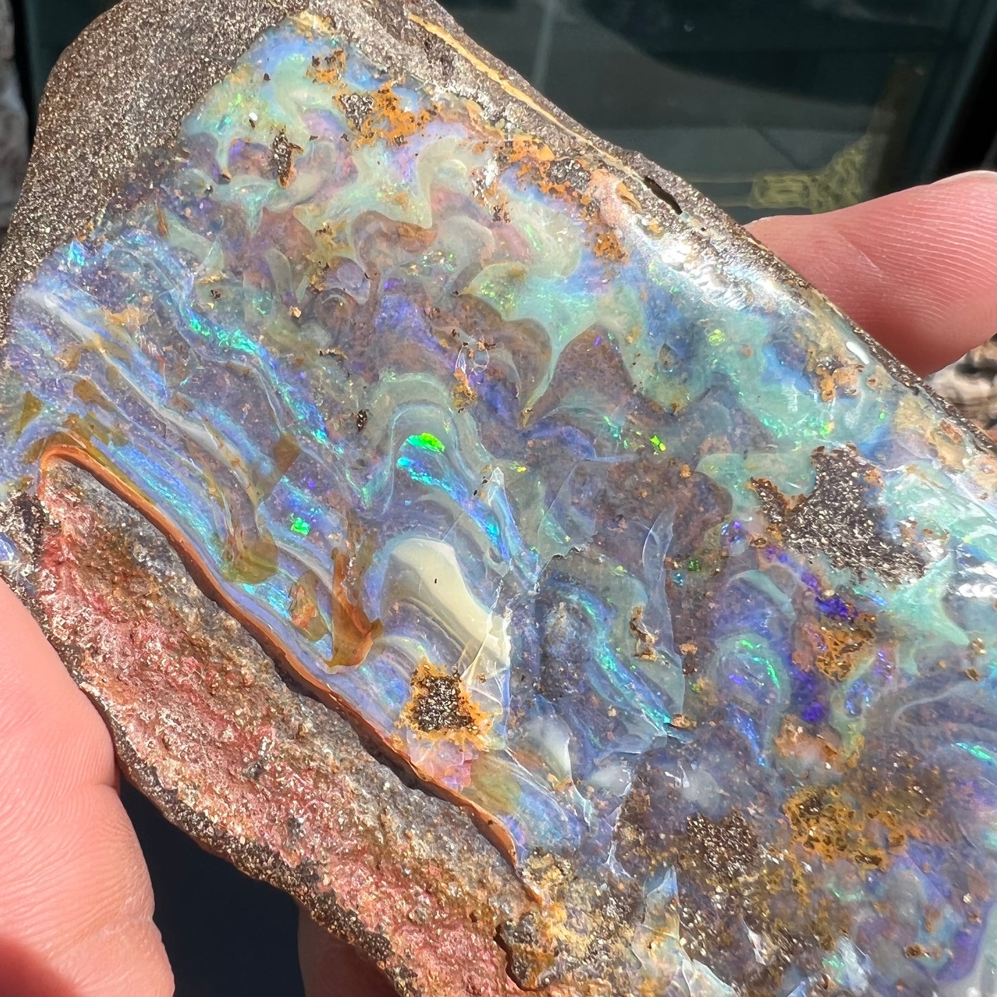 A 7 inch long, polished Quilpie boulder opal specimen. The stone shows colors of blue, green, and orange.