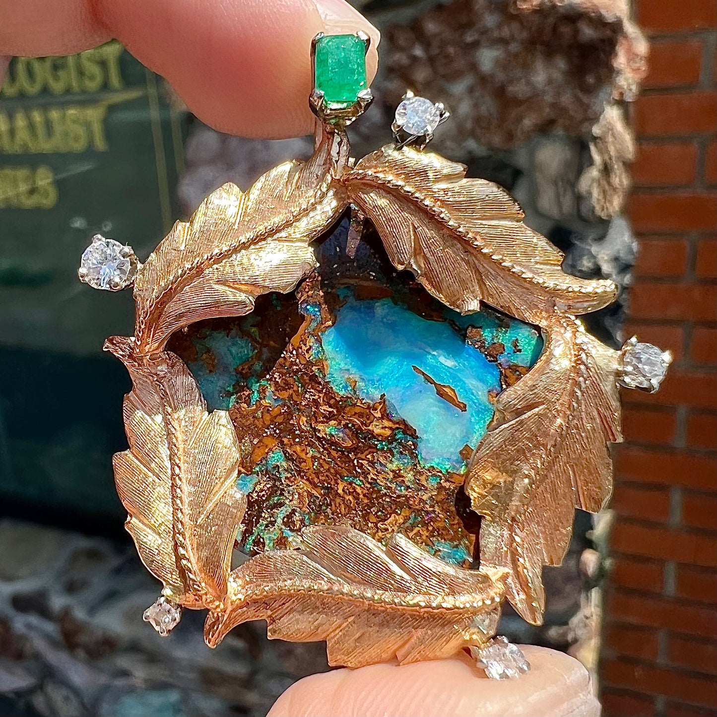 A gold opalized wood, diamond, and emerald pendant. The opal is set in a wreath of gold feathers that form a star.