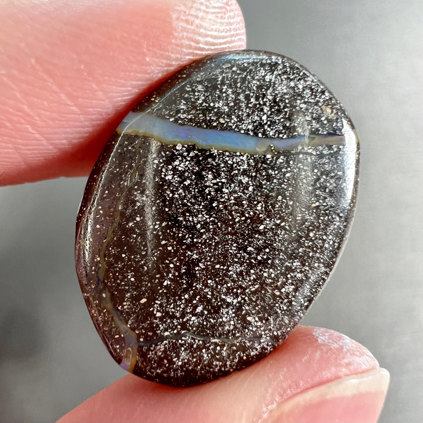 A loose, oval cabochon cut Australian boulder opal stone.