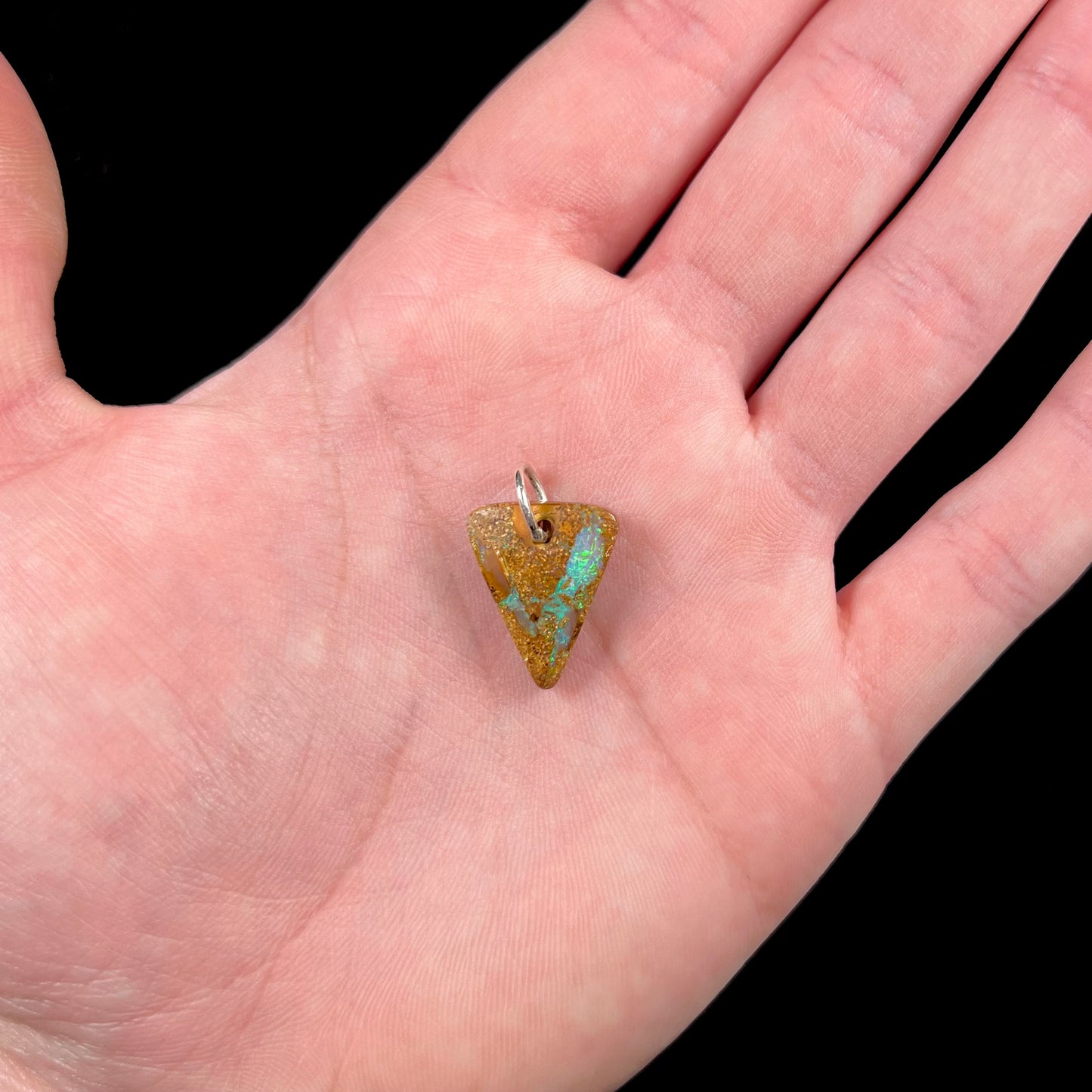 A drilled boulder opal stone with a sterling silver ring through the hole to be worn as a pendant.