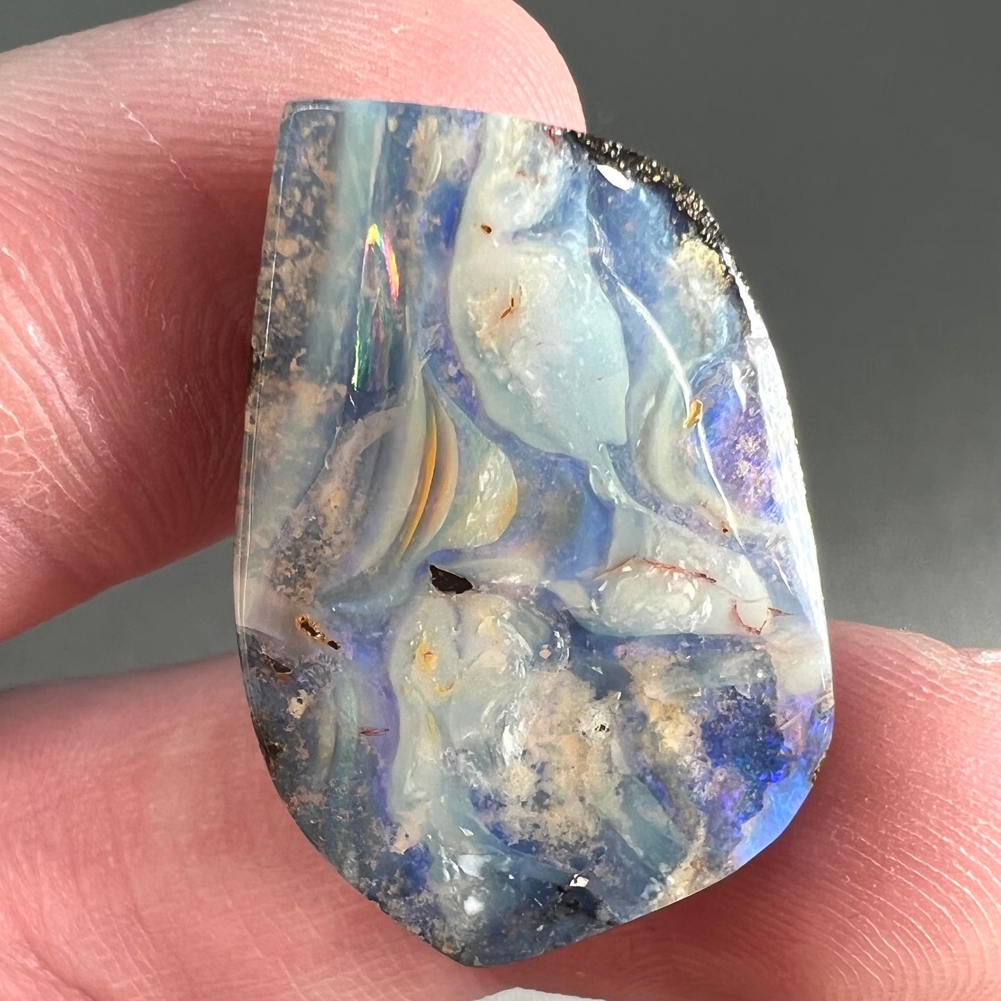 A loose, polished, freeform cut boulder opal stone from Queensland, Australia.