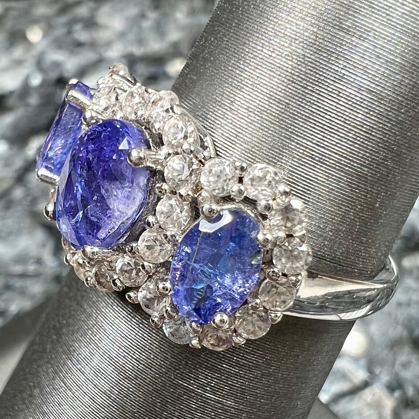 A sterling silver past, present, future three stone tanzanite ring. The main stones are set in a halo of cubic zirconia.