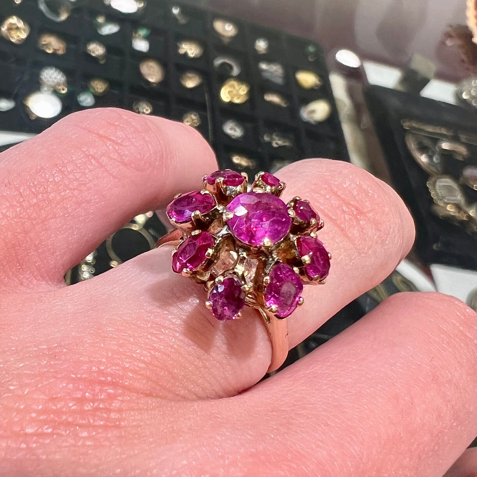 A yellow gold pink Burma ruby cluster ring with a faceted oval center stone surrounded by marquise cut stones.
