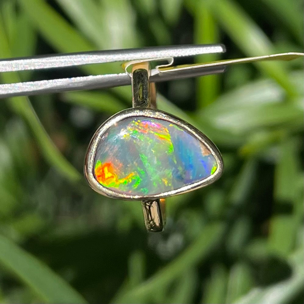 A freeform cut semi-black opal from Lightning Ridge, Australia set in a bezel set yellow gold solitaire ring.