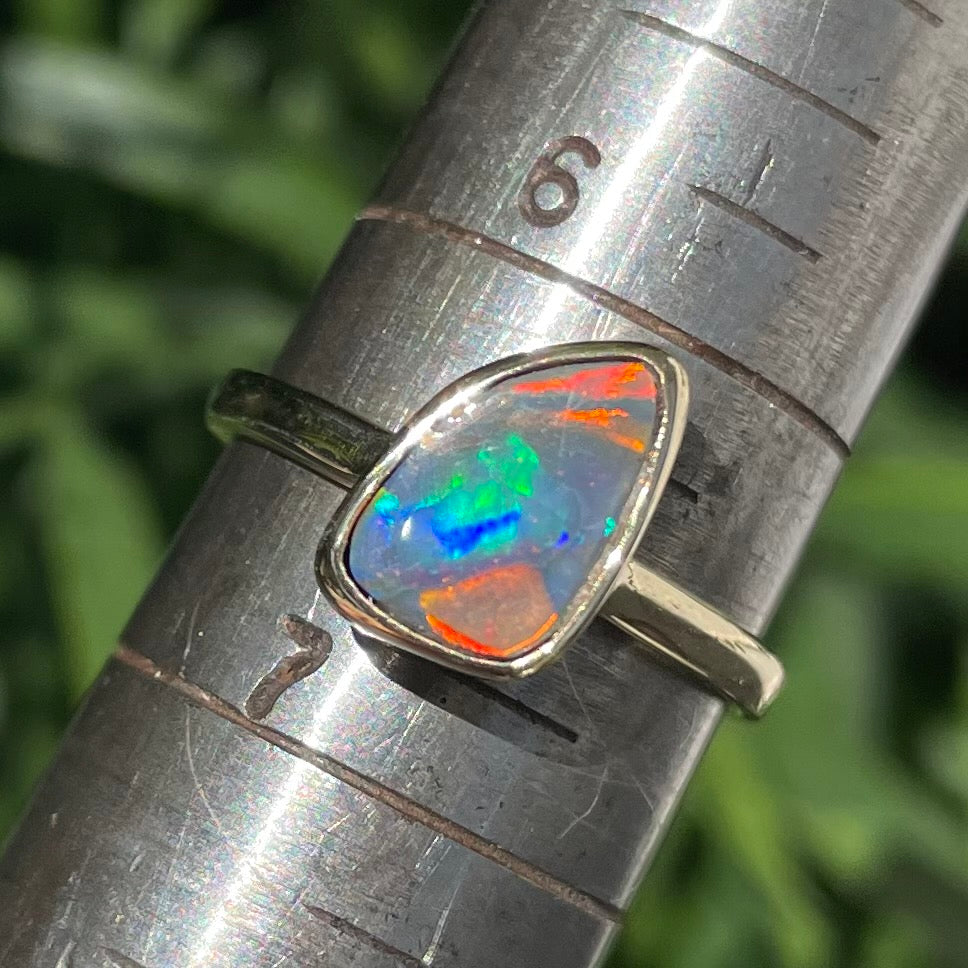 A handmade yellow gold solitaire ring bezel set with a Lightning Ridge red-on-black harlequin opal.