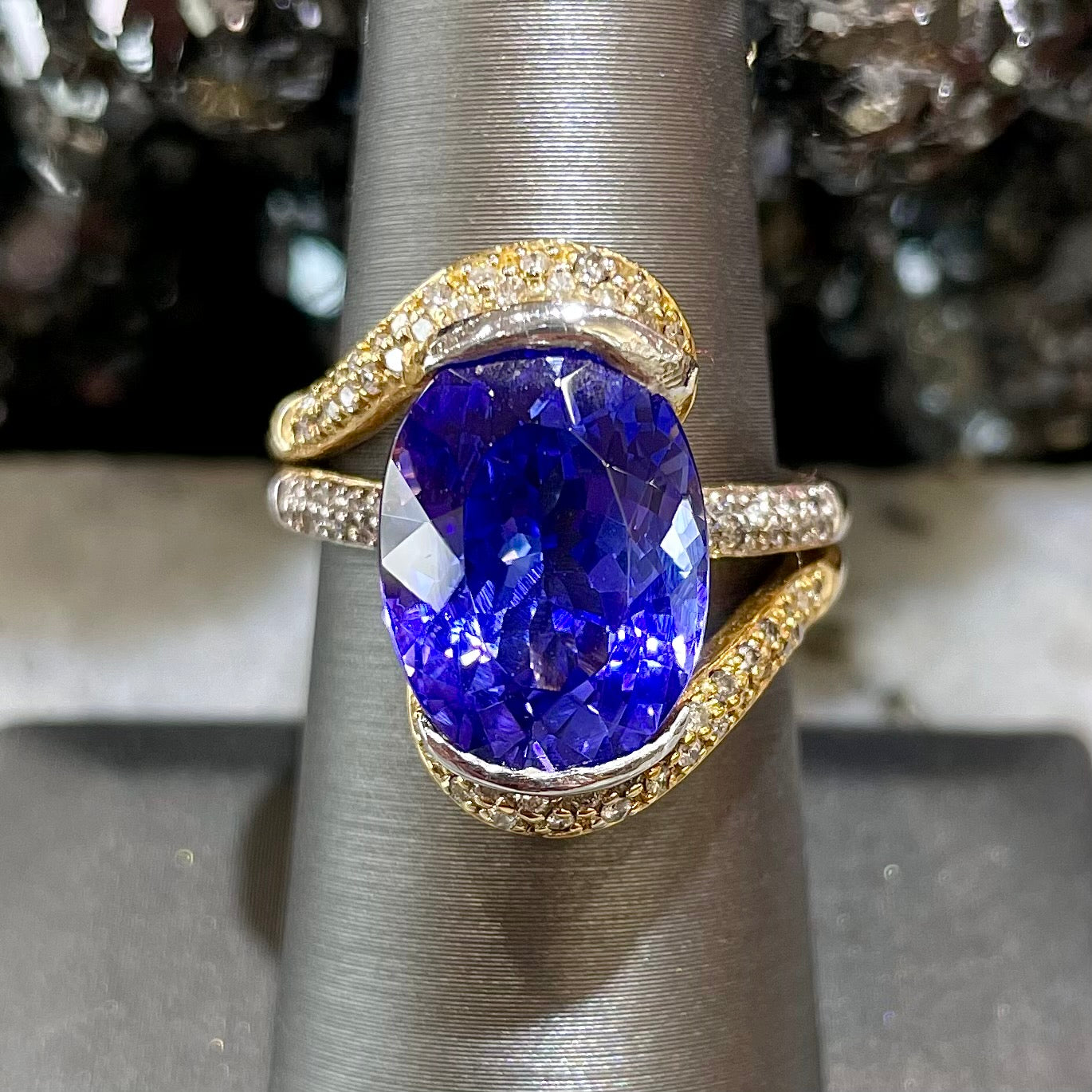 A large, oval cut blue tanzanite set in a two tone yellow and white gold diamond ring.