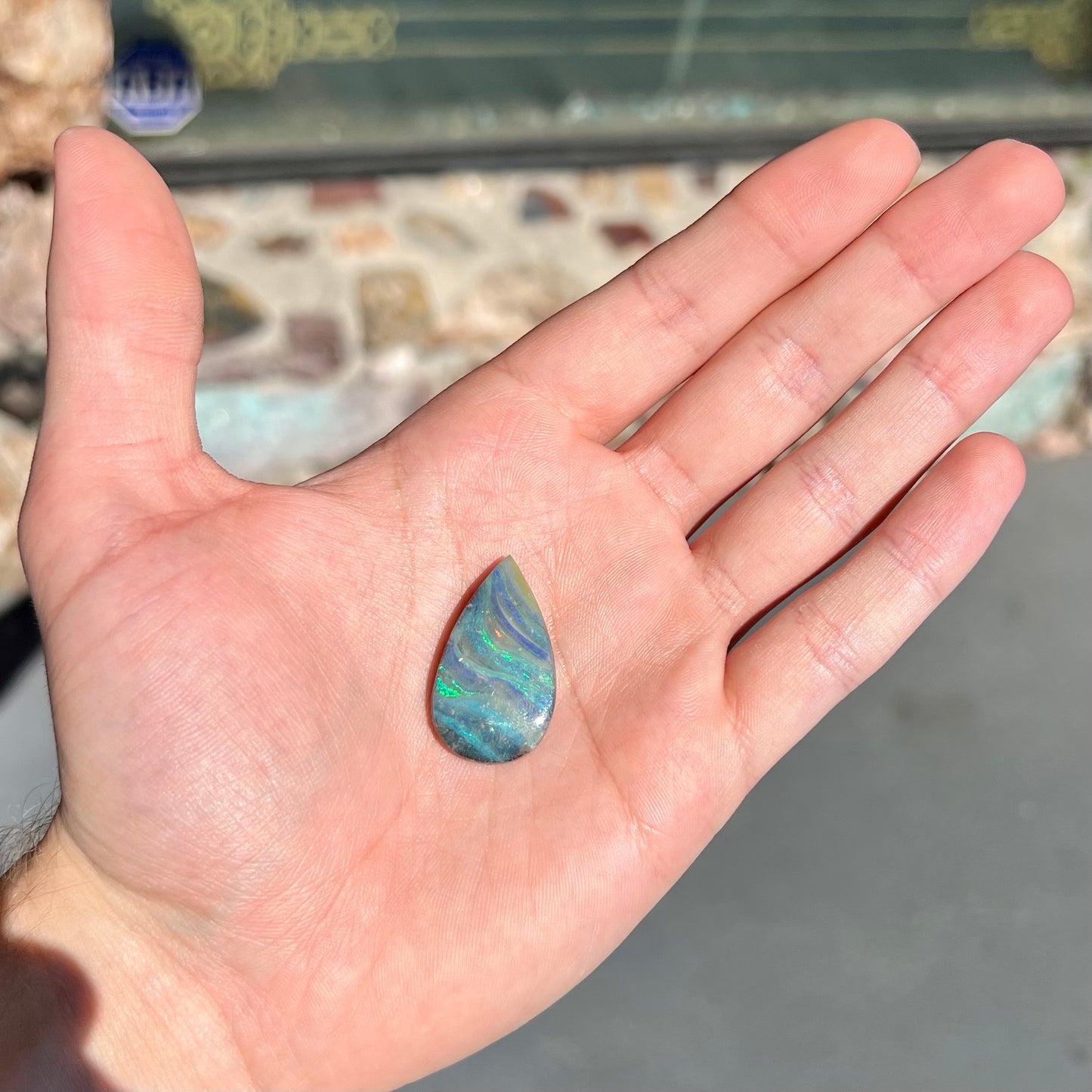 A loose, pear shaped boulder opal stone from Quilpie, Australia. The stone is predominantly blue, green, and purple with red and orange undertones.