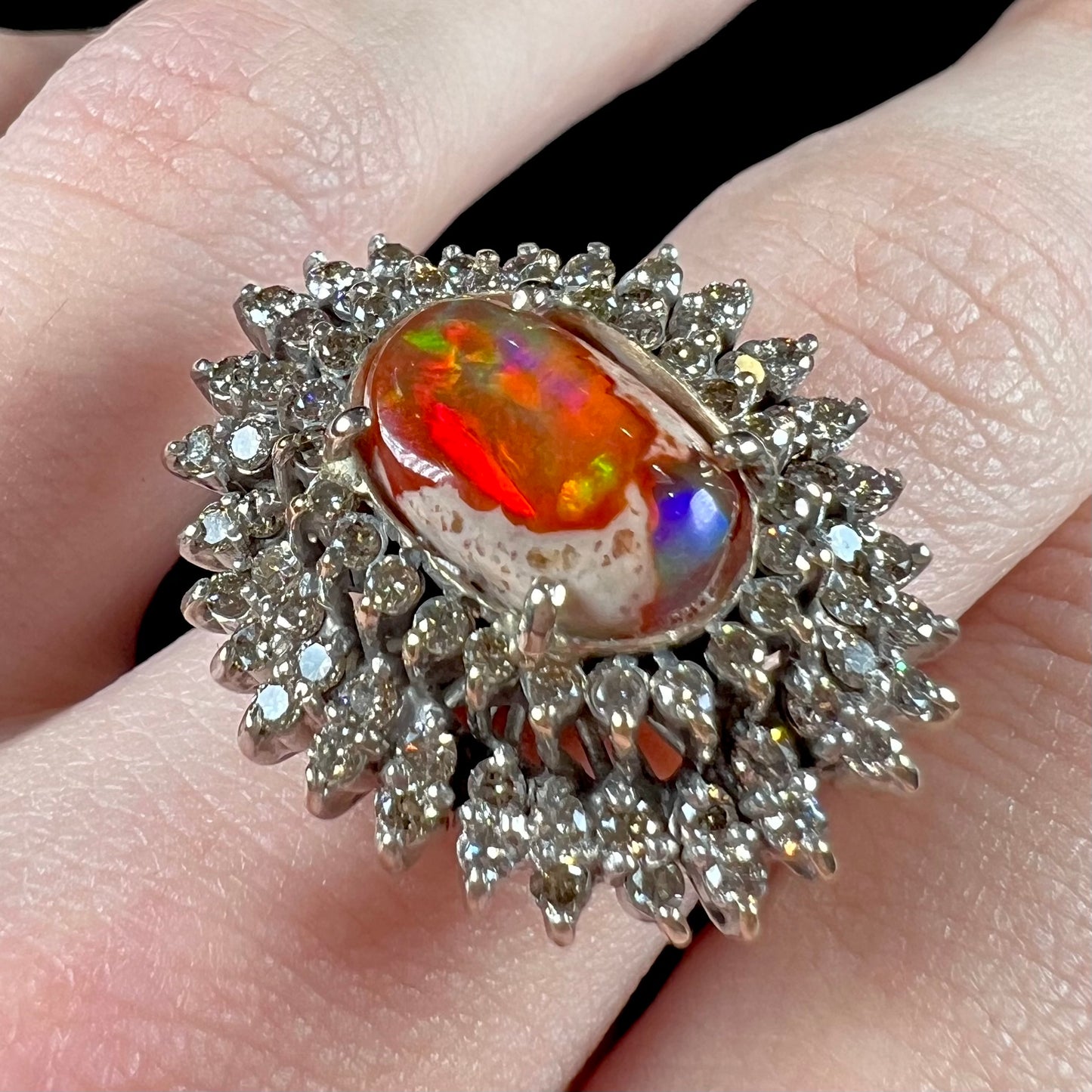 An 18k white gold orange fire opal ring set with a triple halo of diamonds.