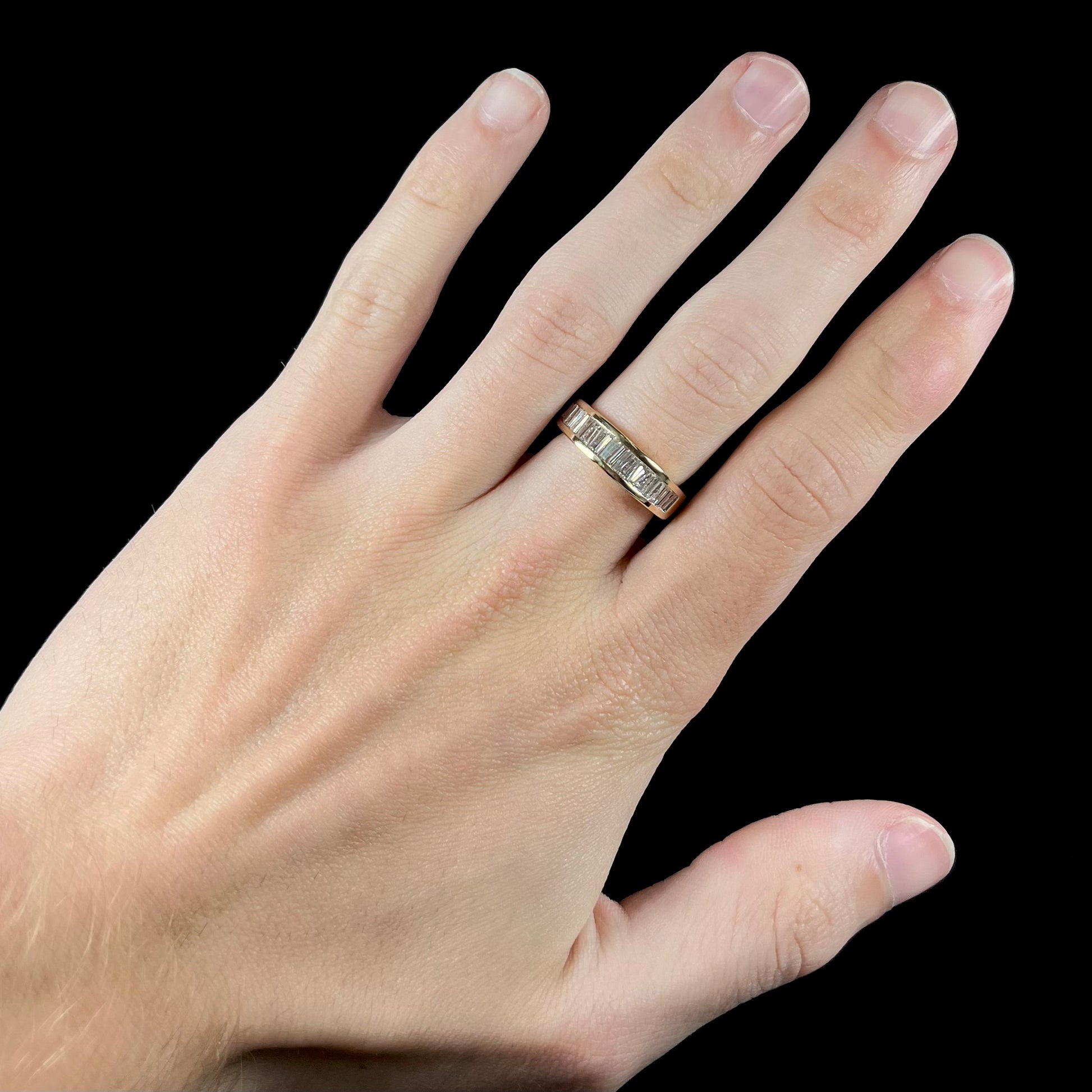 A ladies' yellow gold ring channel set with a row of baguette cut diamonds.