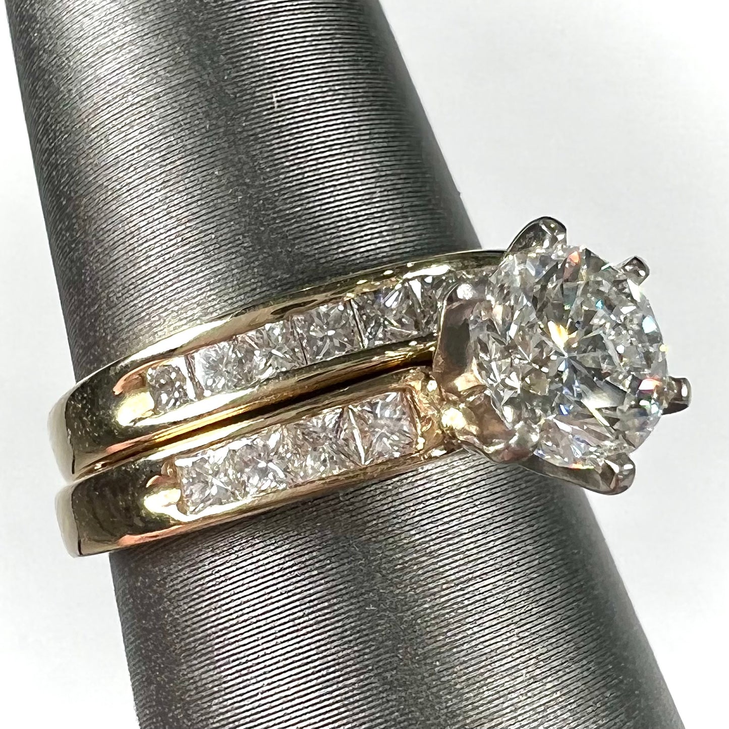 A diamond engagement and wedding ring set. The center stone is a 1 carat round diamond, and the side stones are channel set princess cut diamonds.