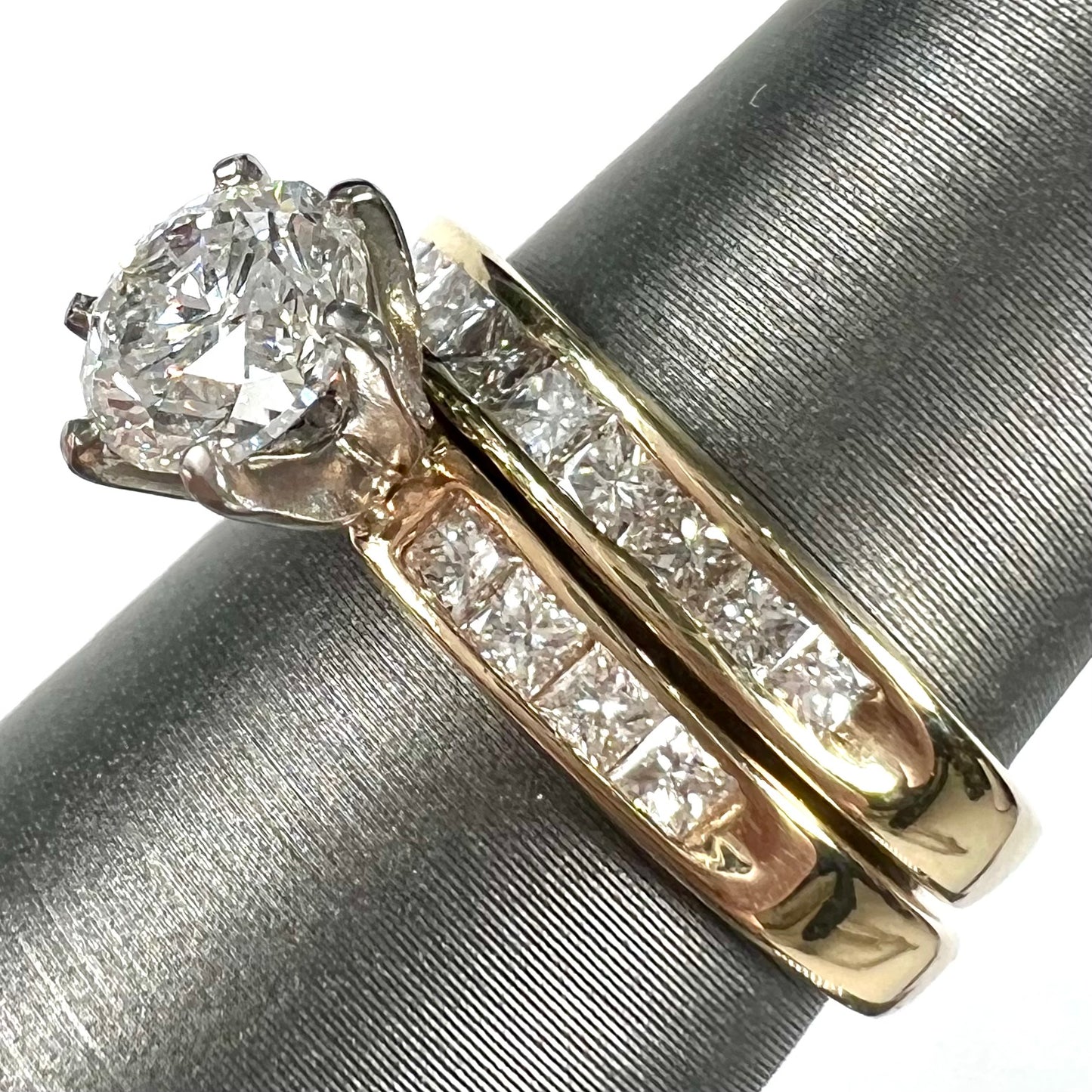 A diamond engagement and wedding ring set. The center stone is a 1 carat round diamond, and the side stones are channel set princess cut diamonds.
