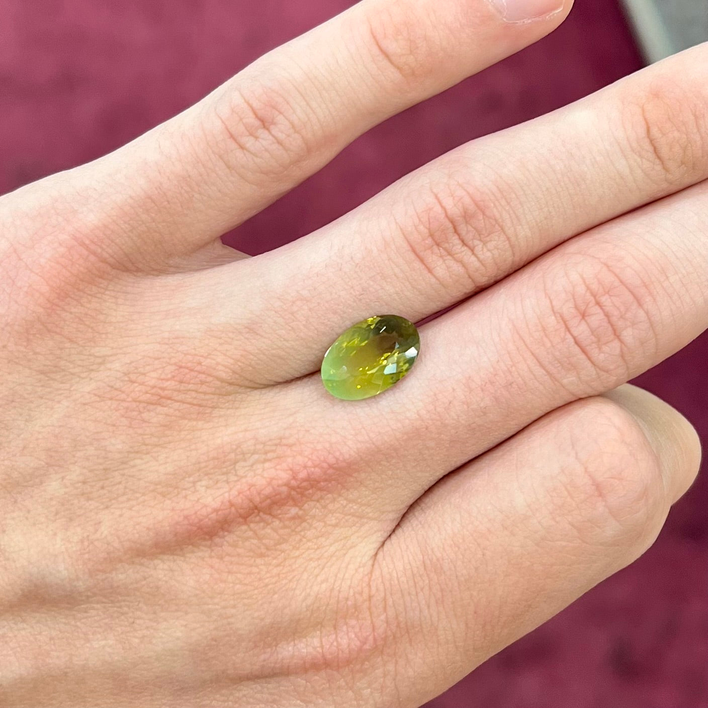 A loose, faceted oval cut bicolor chrysoberyl stone. The stone goes from neon green to dark green with orangey red flashes.