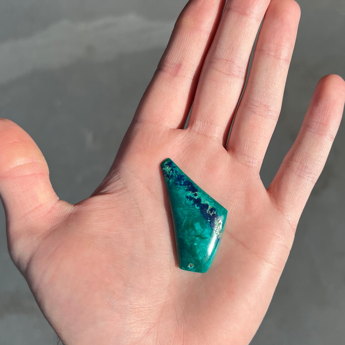 A loose triangular freeform cabochon cut green chrysocolla with blue azurite inclusions.