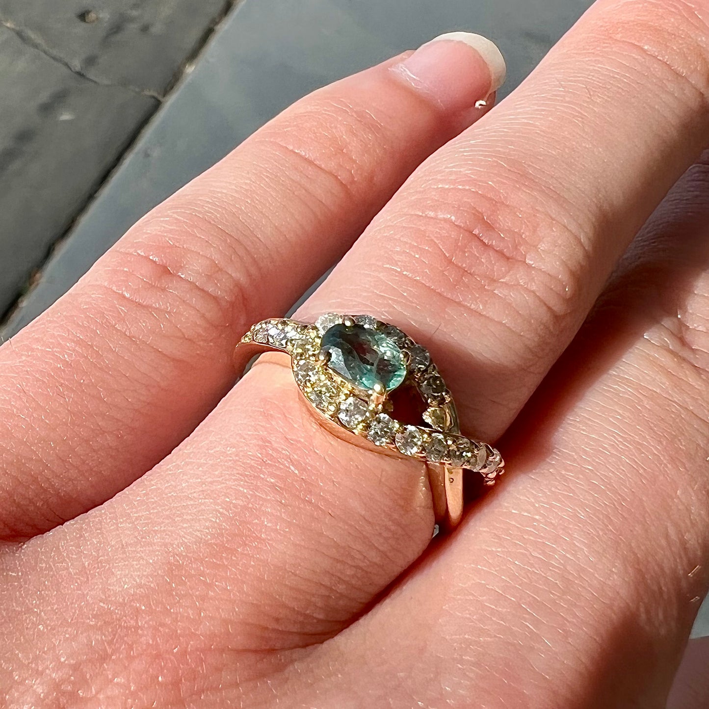 Yellow gold alexandrite and pave set diamond ladies' ring on a hand in natural sunlight.