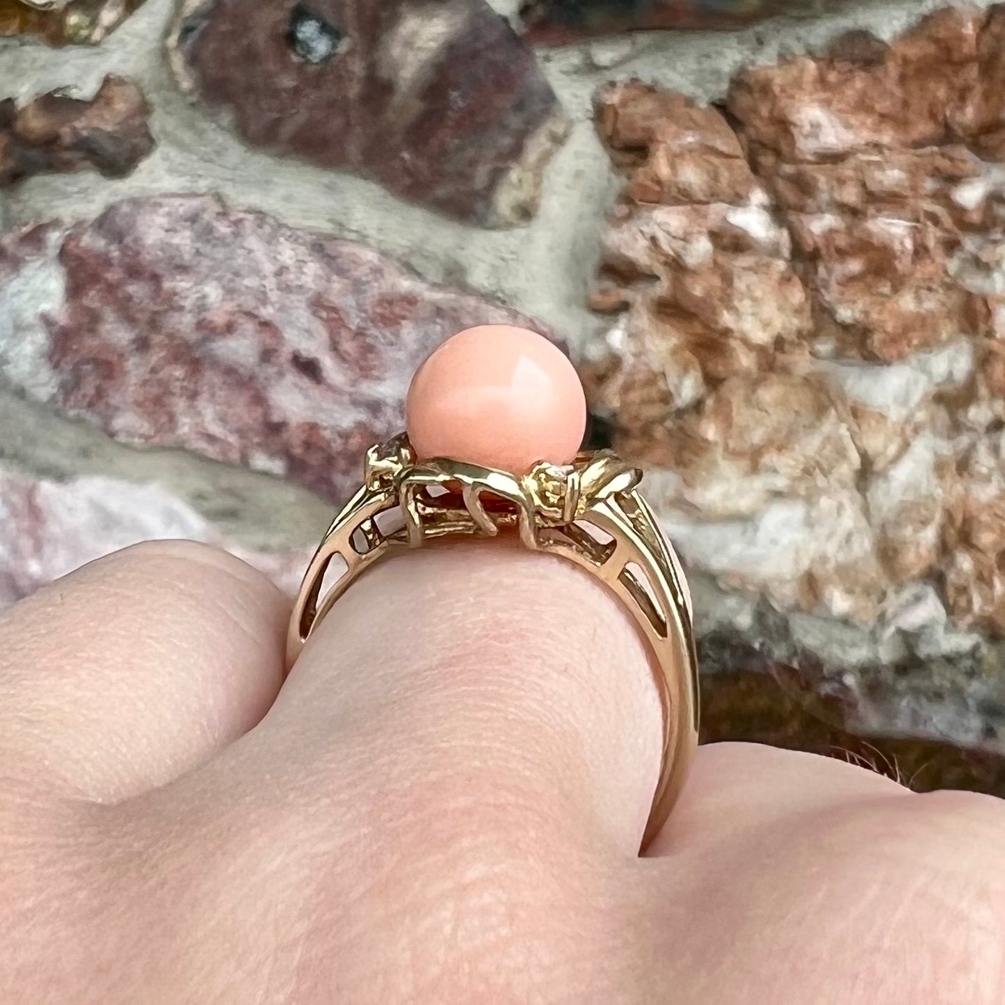 A vintage split shank flower ring set with a round pink coral sphere and diamond accents.