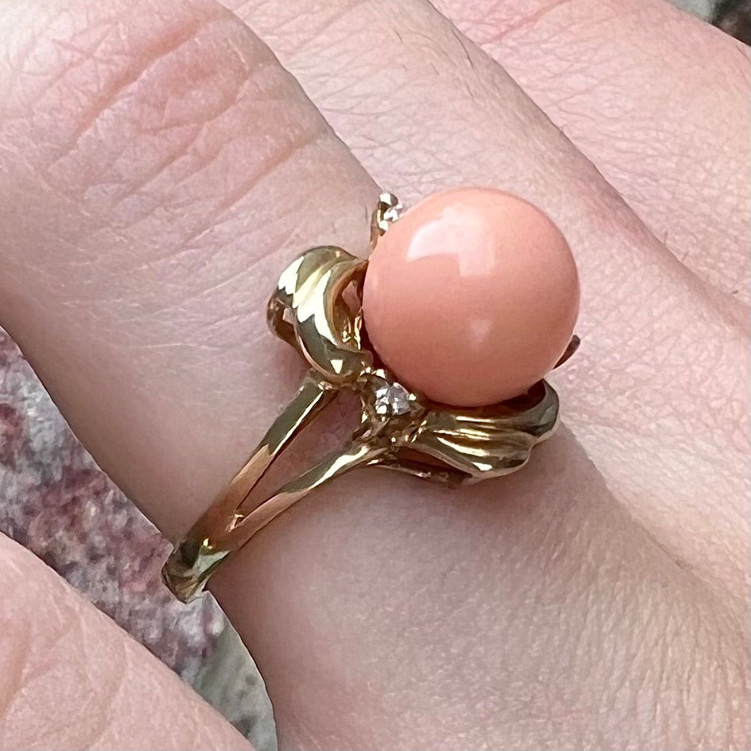 A vintage split shank flower ring set with a round pink coral sphere and diamond accents.
