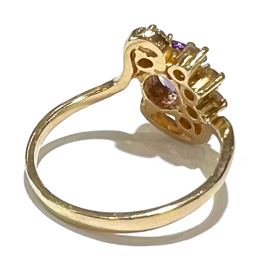 A ring made with 14 karat yellow gold, diamonds, and an amethyst. The ring has a swoosh style.