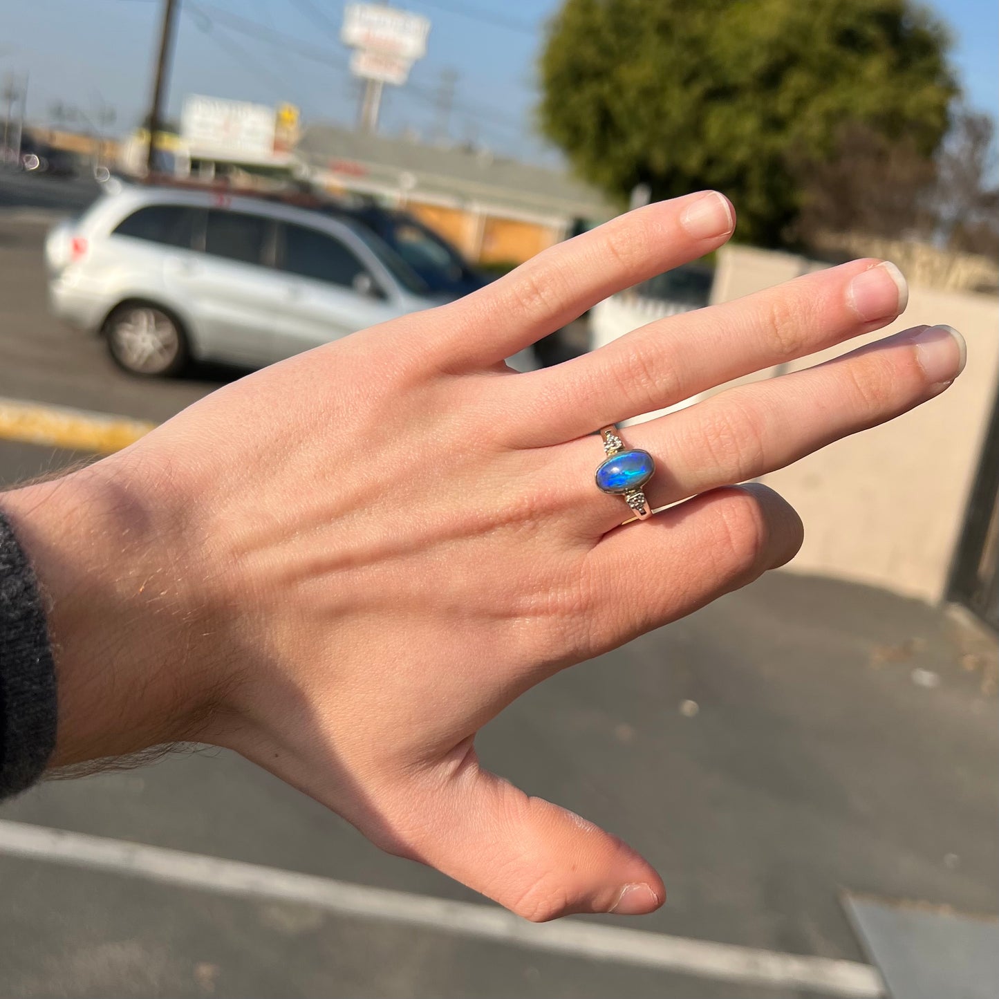 A white gold ring set with a Lightning Ridge black opal and diamond accents. The opal displays a cat's eye pattern.