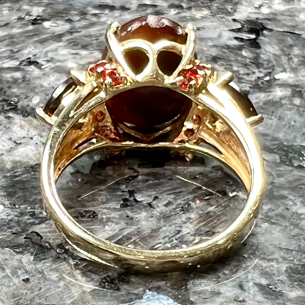A ladies yellow gold fire agate ring set with trillion cut smoky quartz and round cut red-orange garnet accents. The fire agate displays green and red.
