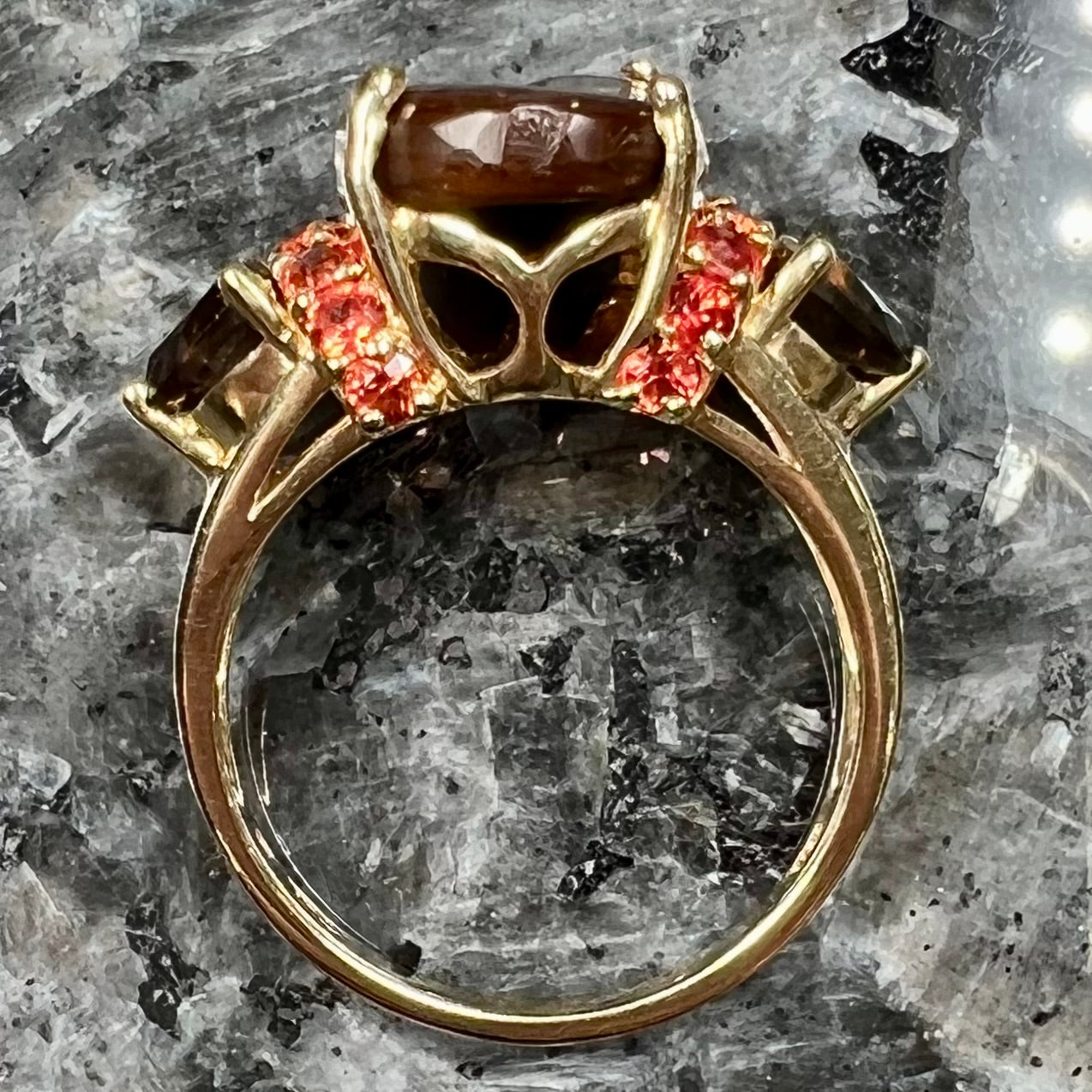 A ladies yellow gold fire agate ring set with trillion cut smoky quartz and round cut red-orange garnet accents. The fire agate displays green and red.