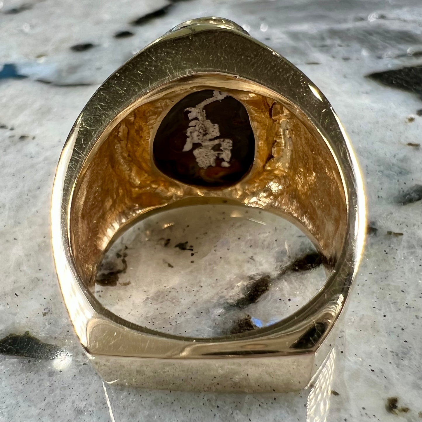 A solid, yellow gold men's fire agate ring. The predominant color is red with green undertones.