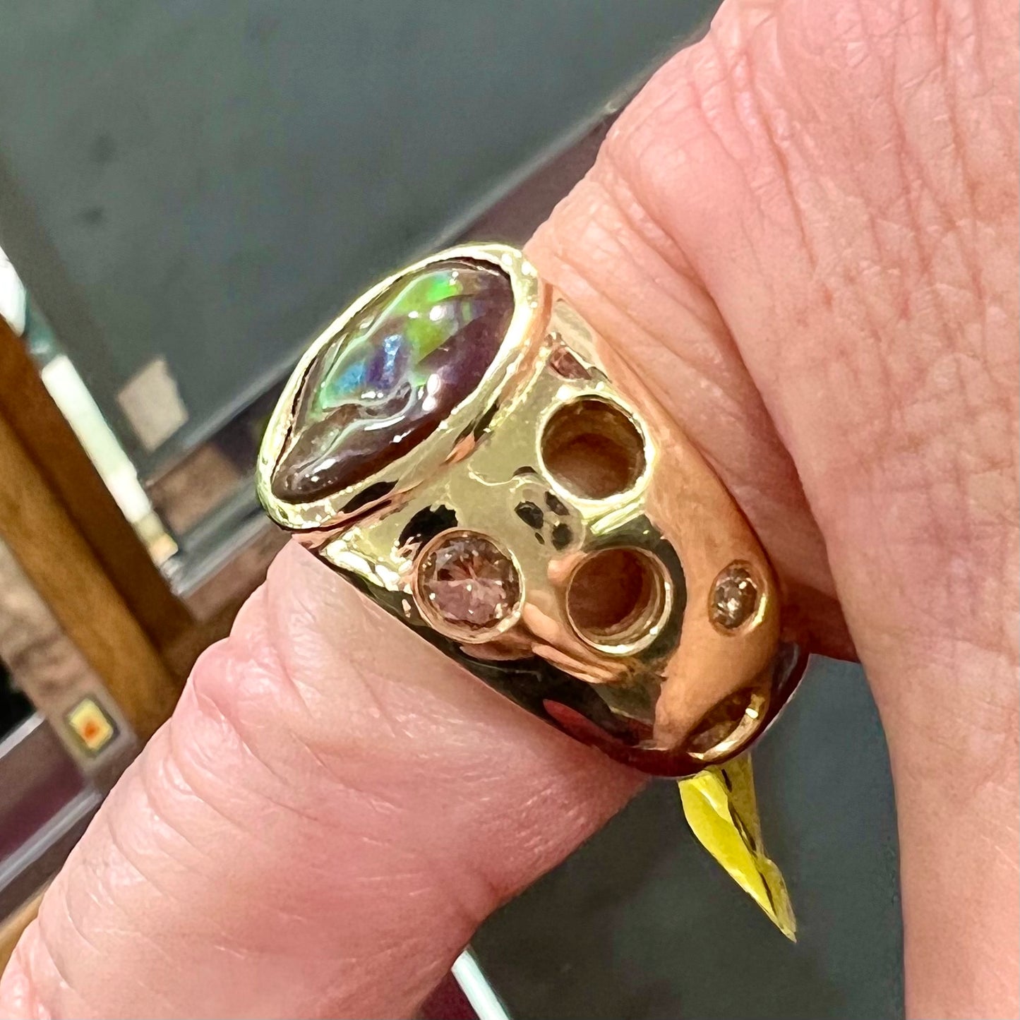 Men's rainbow fire agate ring set in yellow gold with champagne diamonds. The ring style has holes.