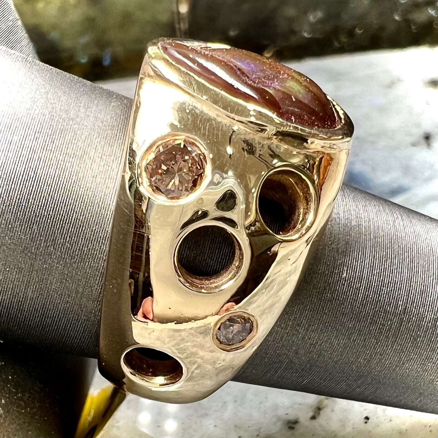 Men's rainbow fire agate ring set in yellow gold with champagne diamonds. The ring style has holes.