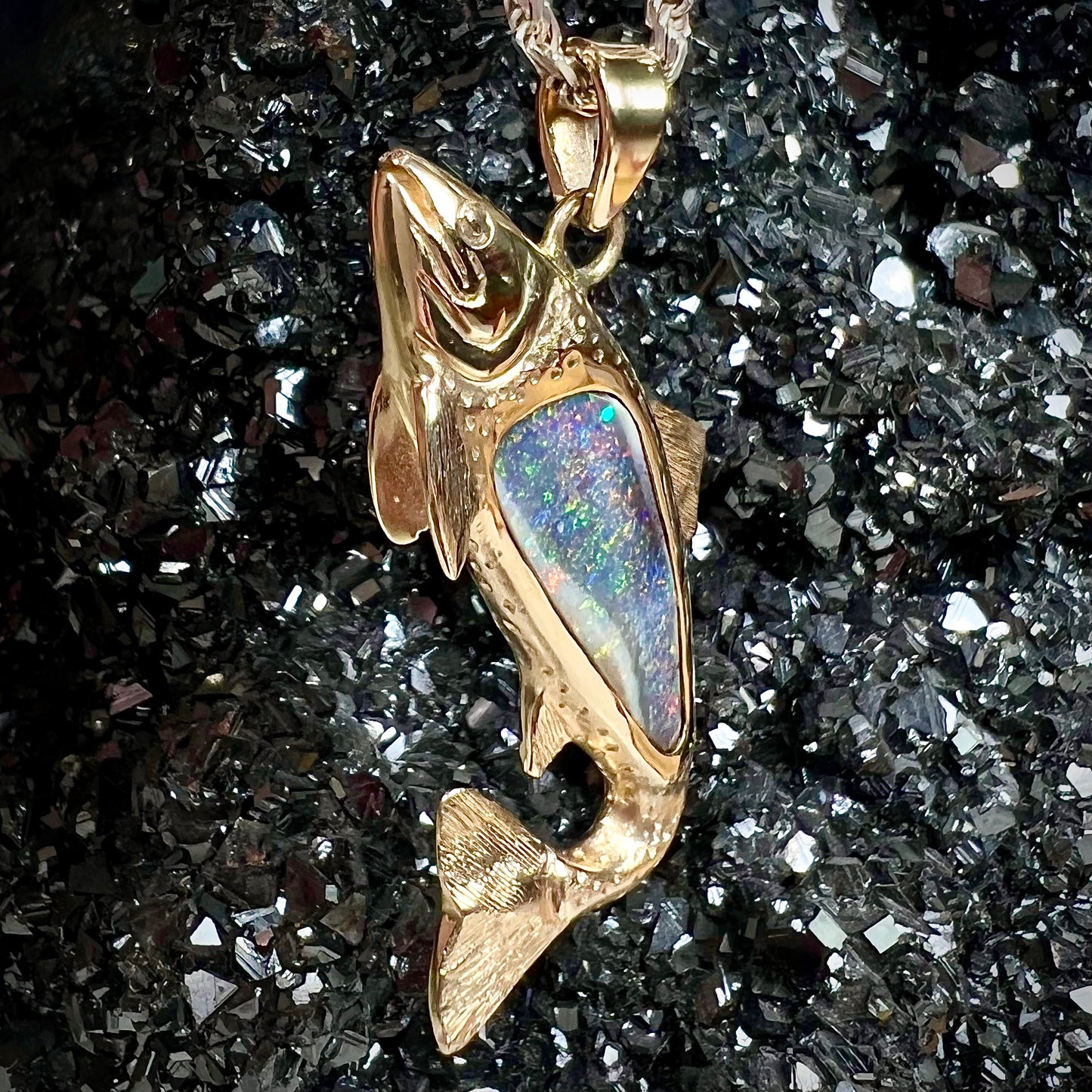 A yellow gold fish pendant detailed to look like a rainbow trout. The body of the fish is set with a color changing black opal stone.