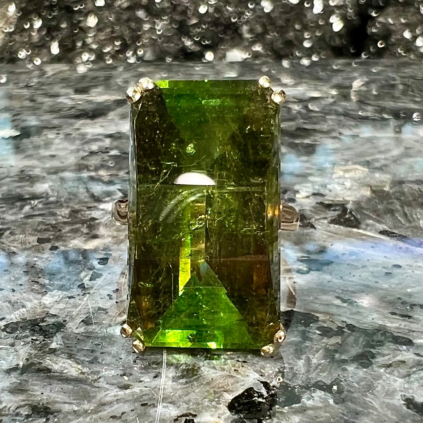 A faceted step-cut dark green tourmaline basket set solitaire ring cast in yellow gold.