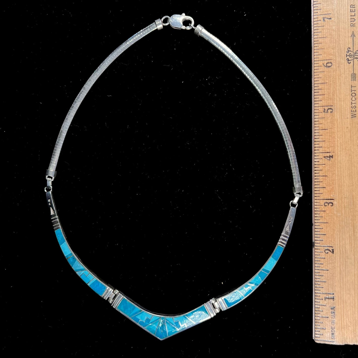 A silver omega style necklace inlaid with turquoise under the watch of David Rosales.