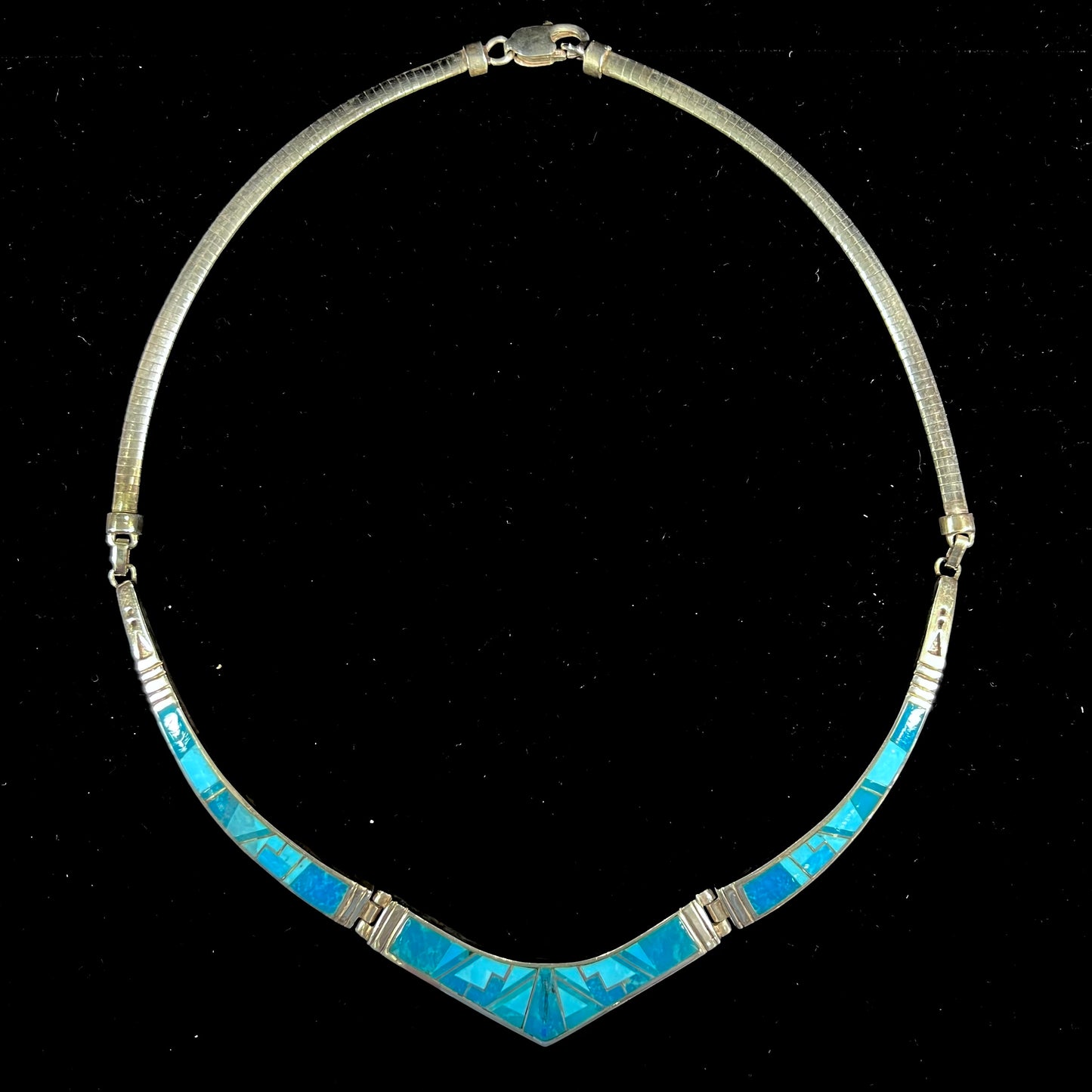 A silver omega style necklace inlaid with turquoise under the watch of David Rosales.