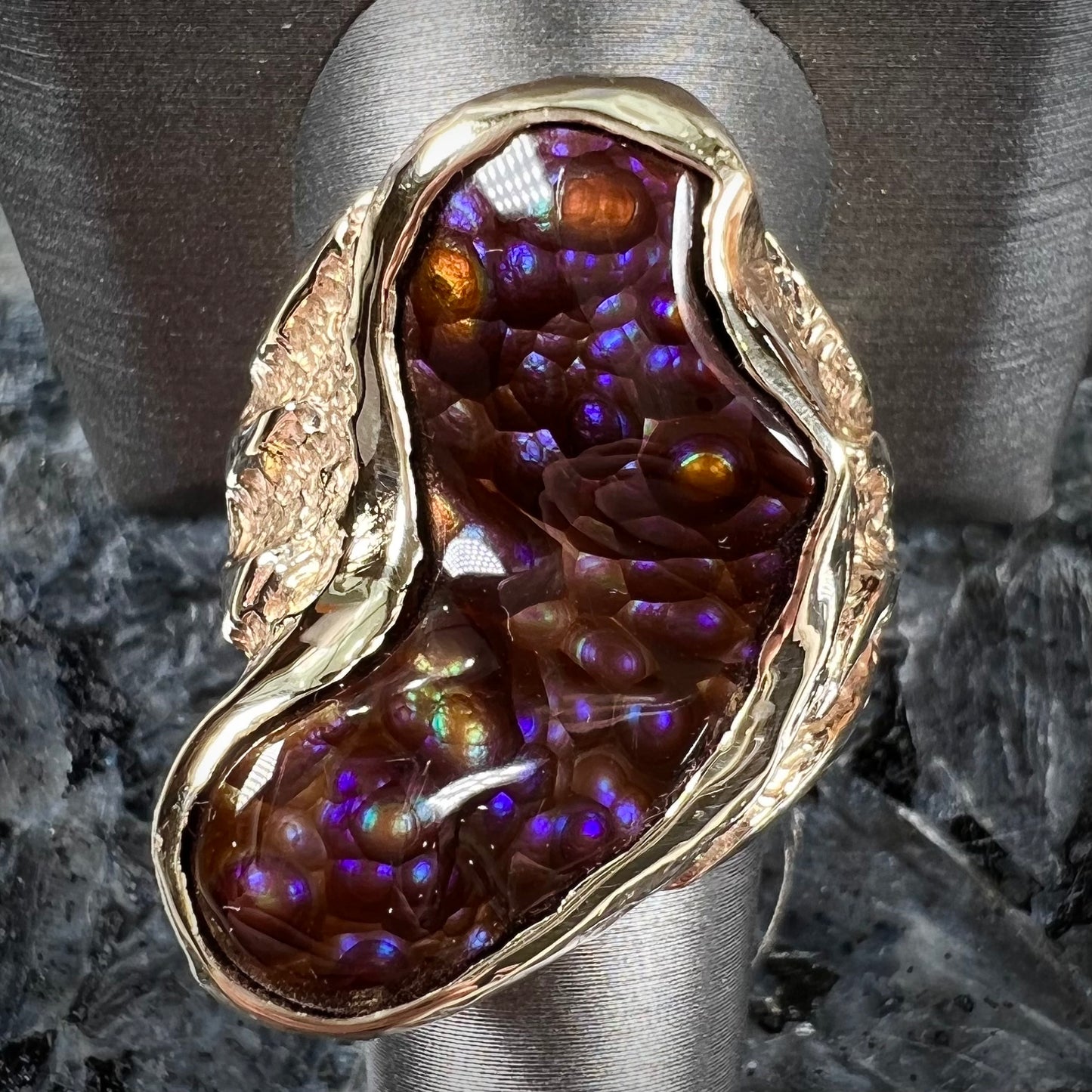 A men's Deer Creek fire agate solitaire ring cast in yellow gold. The stone is predominantly purple.