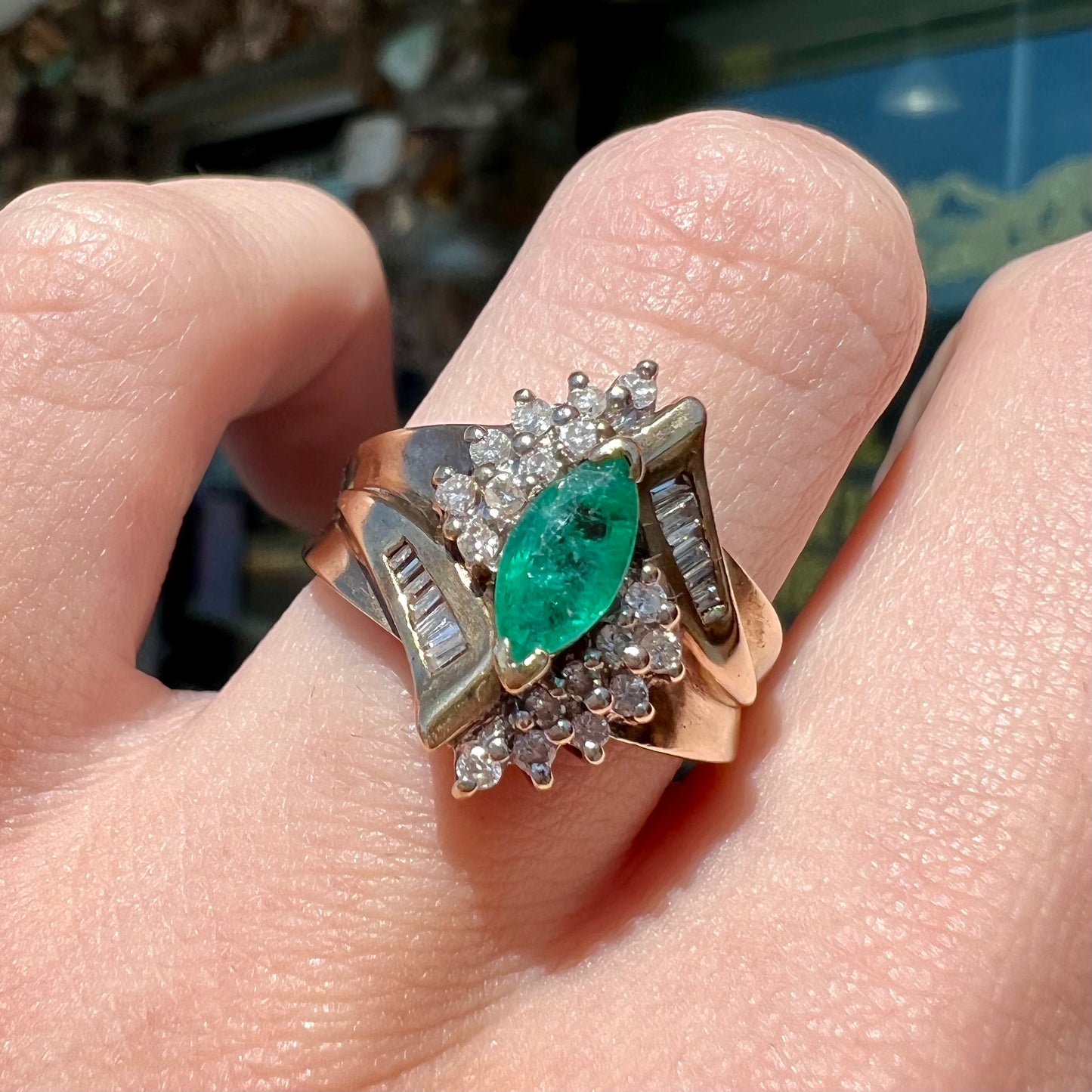 A yellow gold marquise cut emerald and diamond ring. The diamonds are prong set round cuts and channel set baguette cuts.