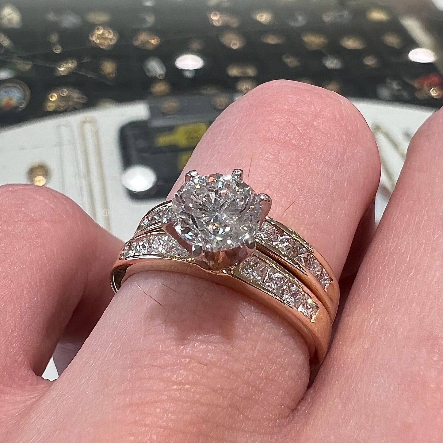 A diamond engagement and wedding ring set. The center stone is a 1 carat round diamond, and the side stones are channel set princess cut diamonds.