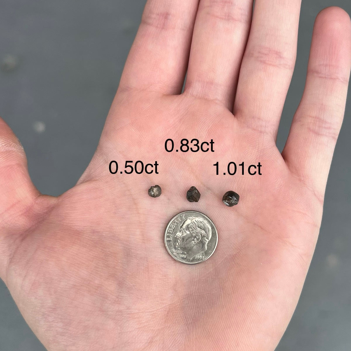 Three different sizes of rough black diamond crystal compared with a US dime.