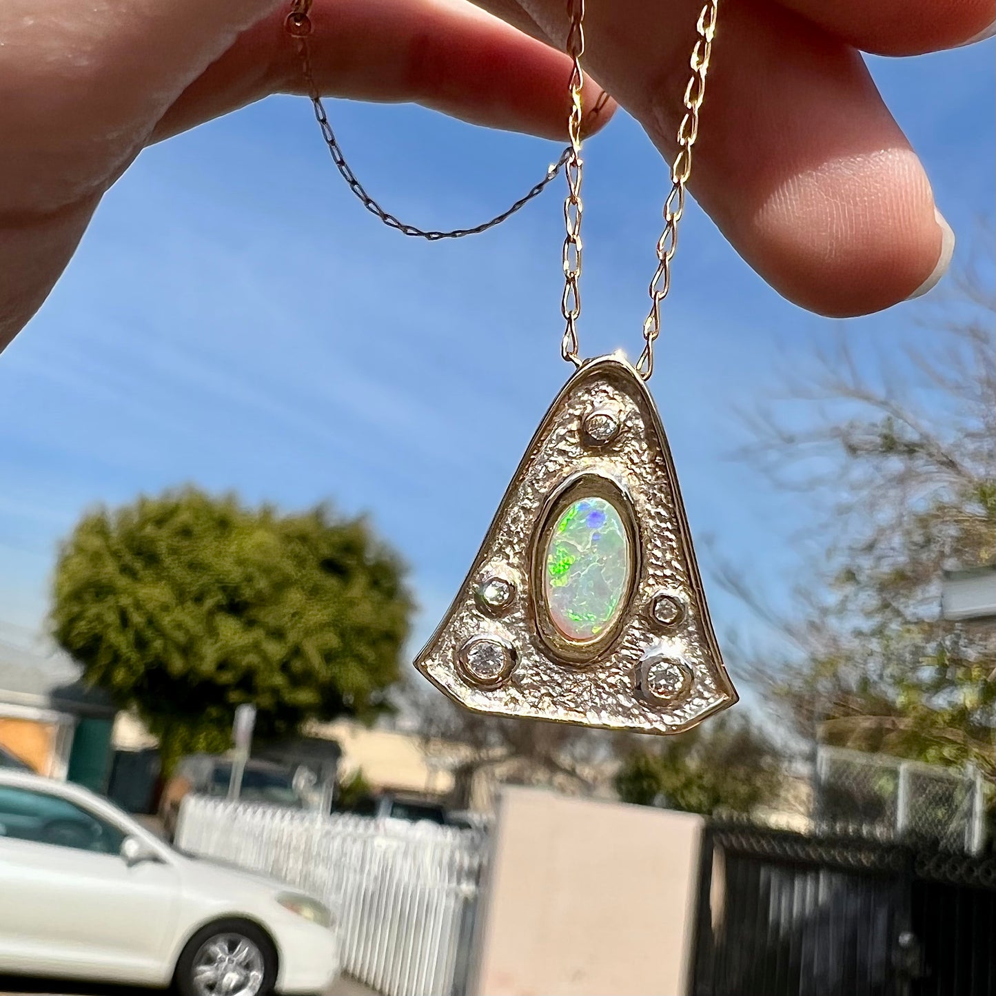 A triangular gold pendant set with five round diamonds and a white crystal opal with green fire.