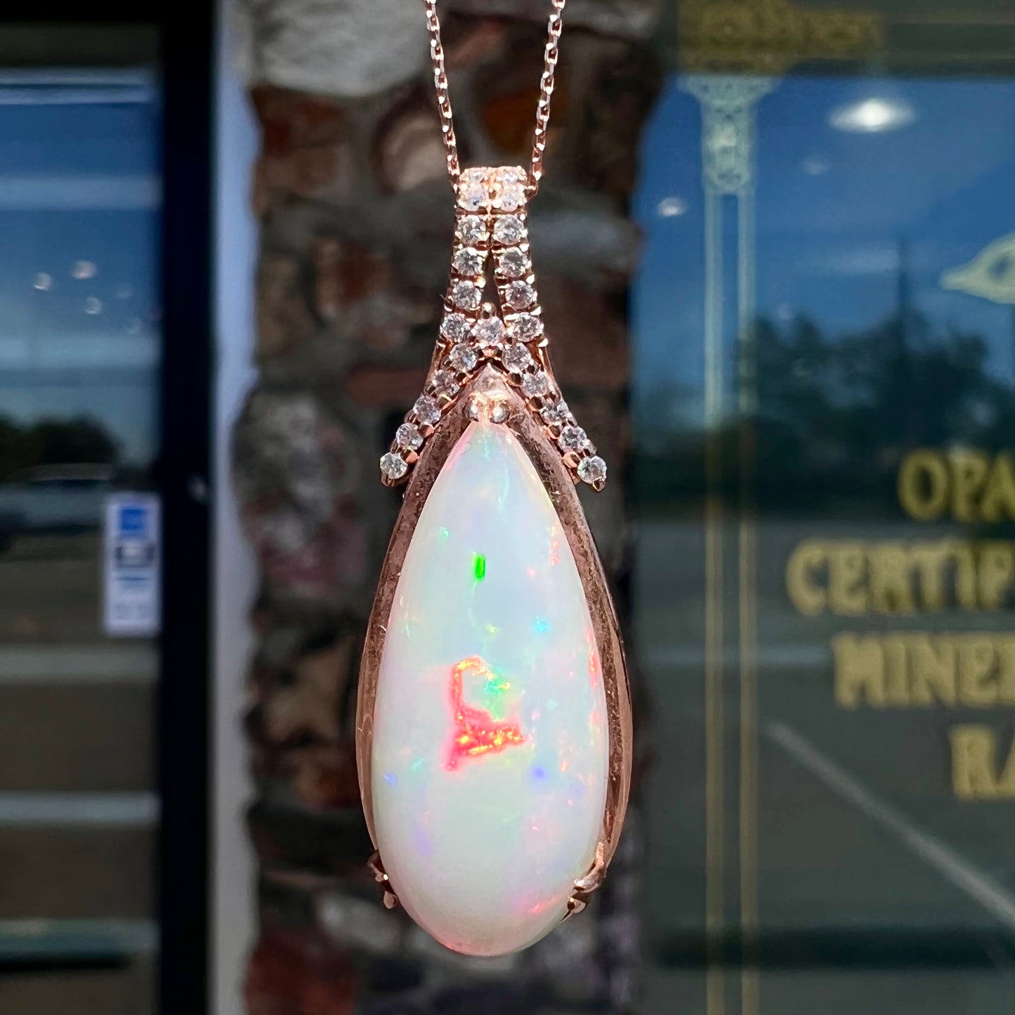 A rose gold, teardrop shaped fire opal and diamond necklace on a cable chain.