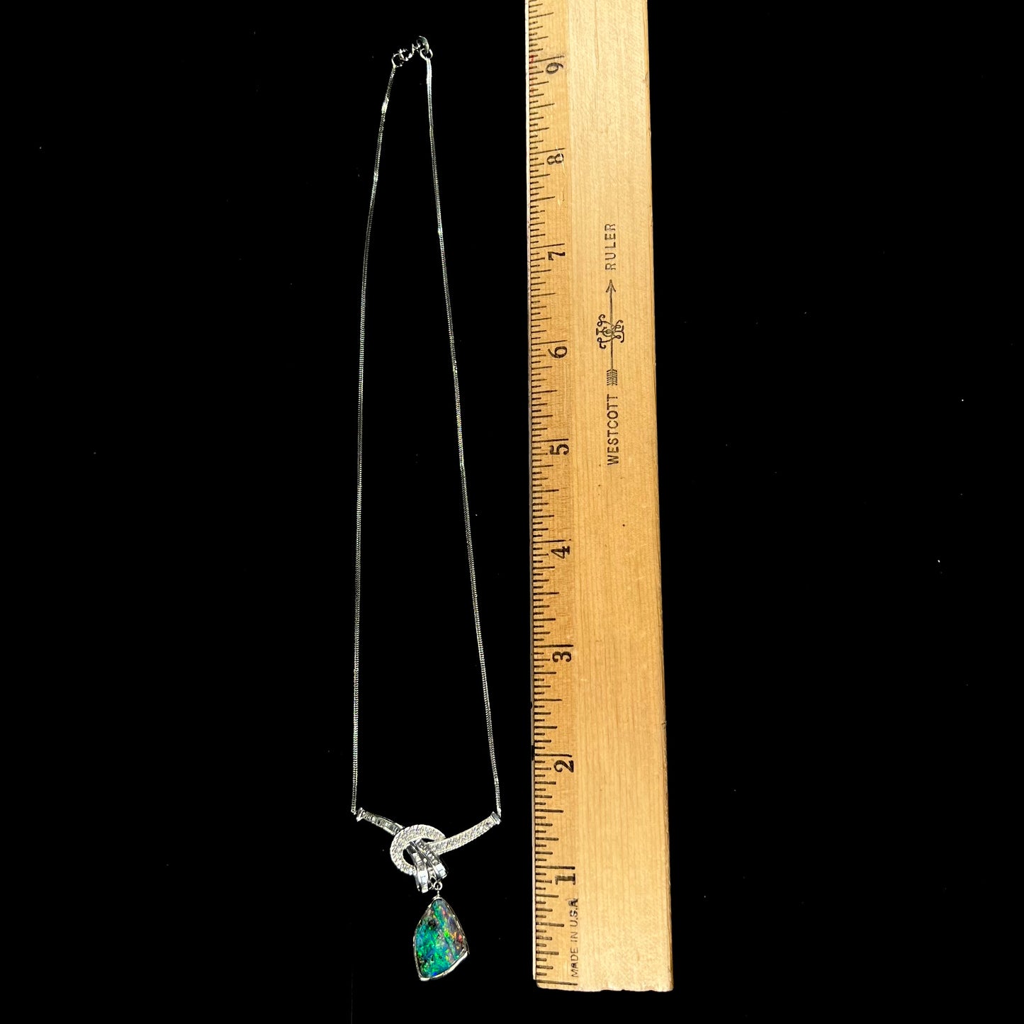 A white gold necklace set with diamonds and a dangling, bezel set boulder opal.