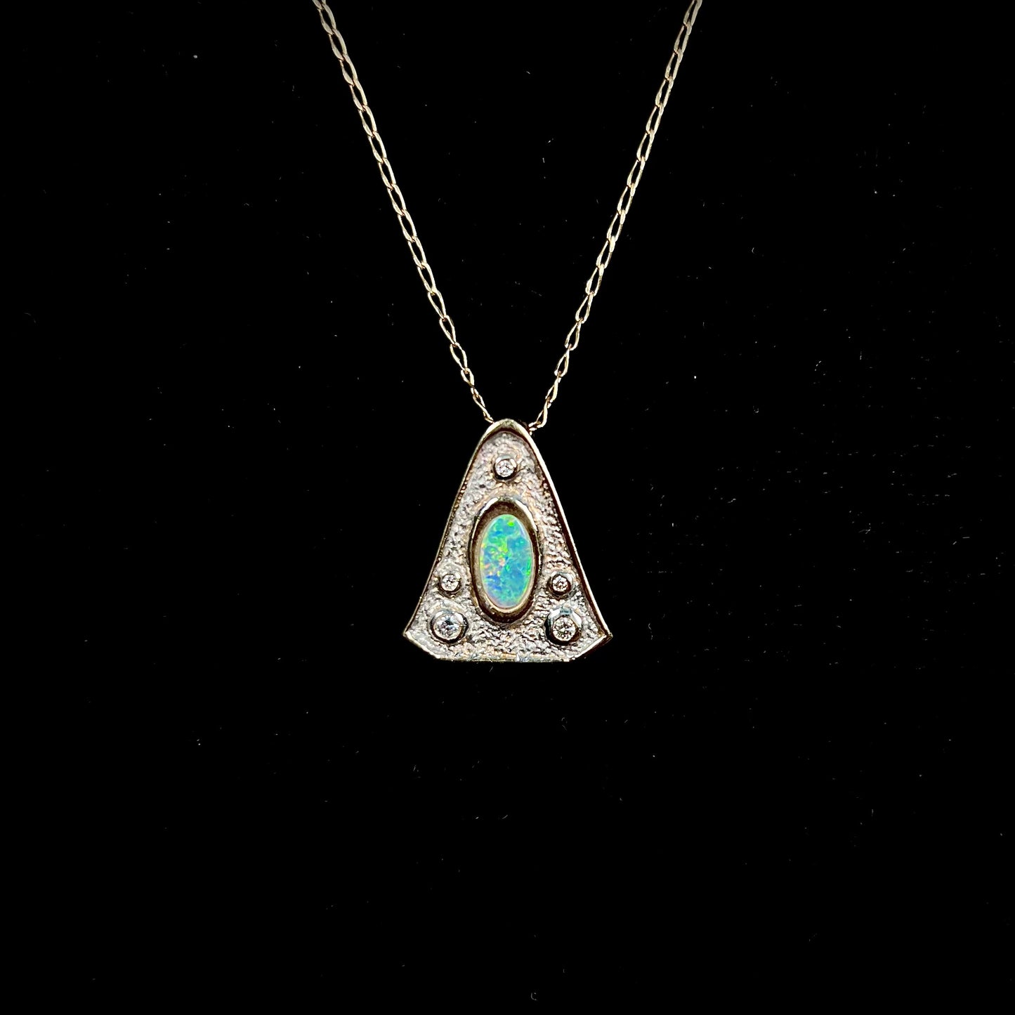 A triangular gold pendant set with five round diamonds and a white crystal opal with green fire.