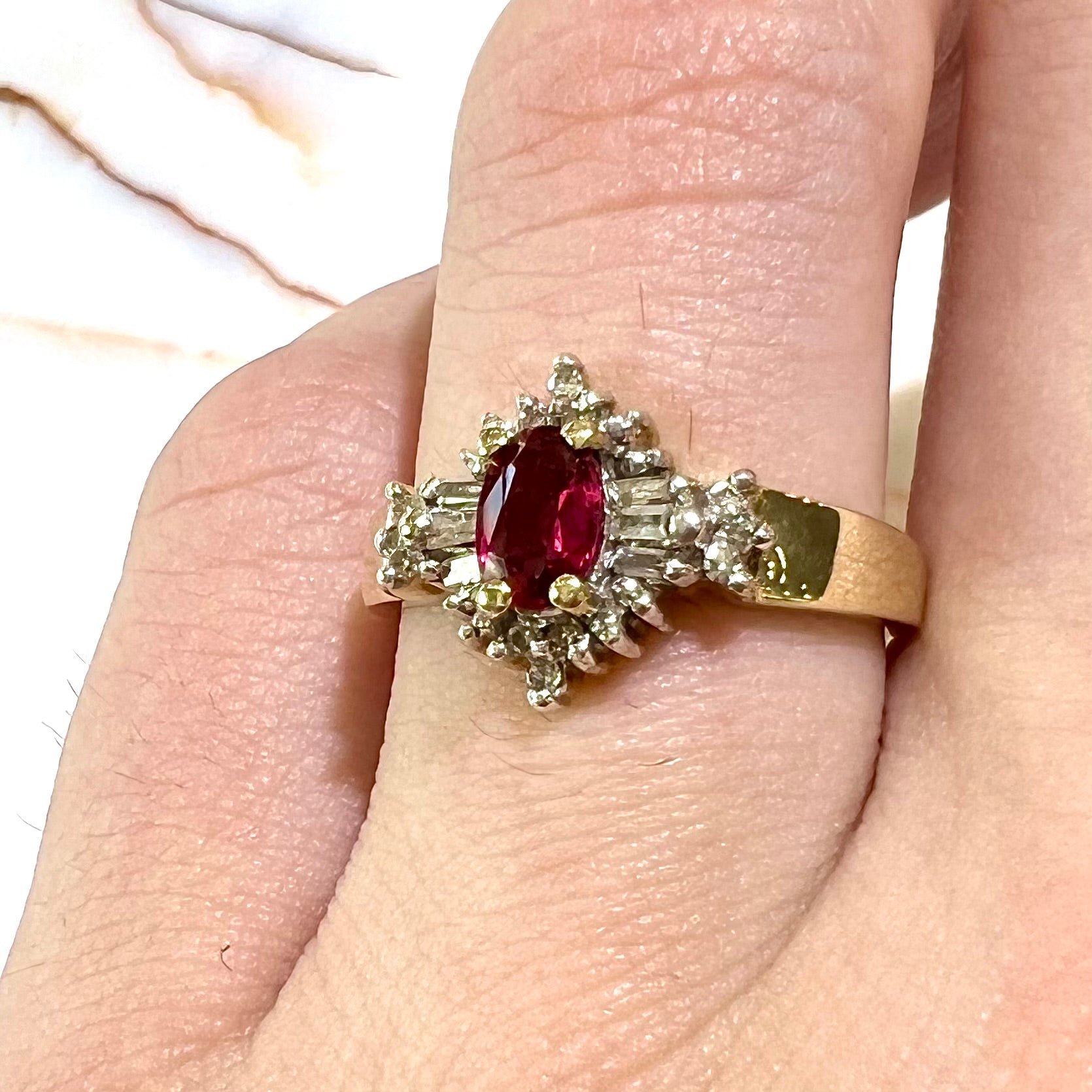 A yellow gold ring set with an oval cut red spinel and diamond rounds and baguettes.