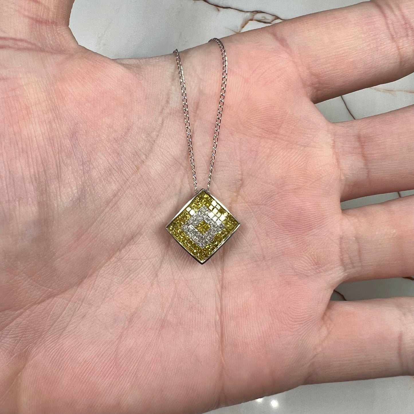 A square shaped necklace set with princess cut yellow and white diamonds in a white gold setting on a white gold chain.