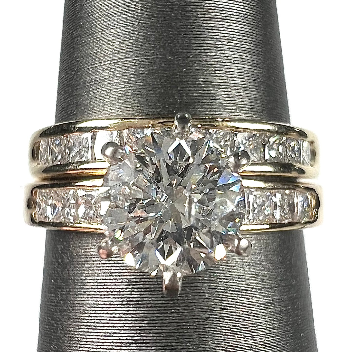 A diamond engagement and wedding ring set. The center stone is a 1 carat round diamond, and the side stones are channel set princess cut diamonds.