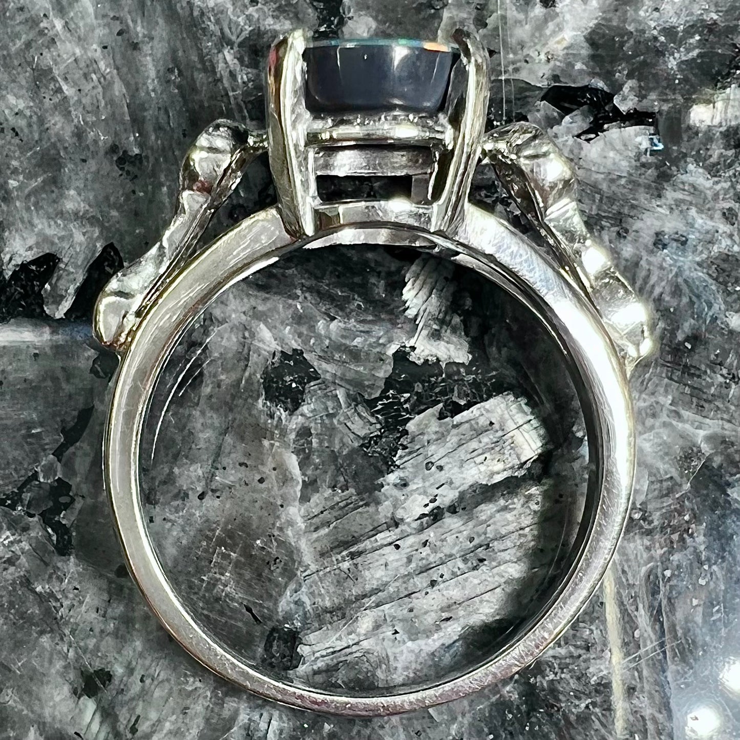 A white gold, oval cabochon cut black opal doublet ring set with two round diamond accent stones.