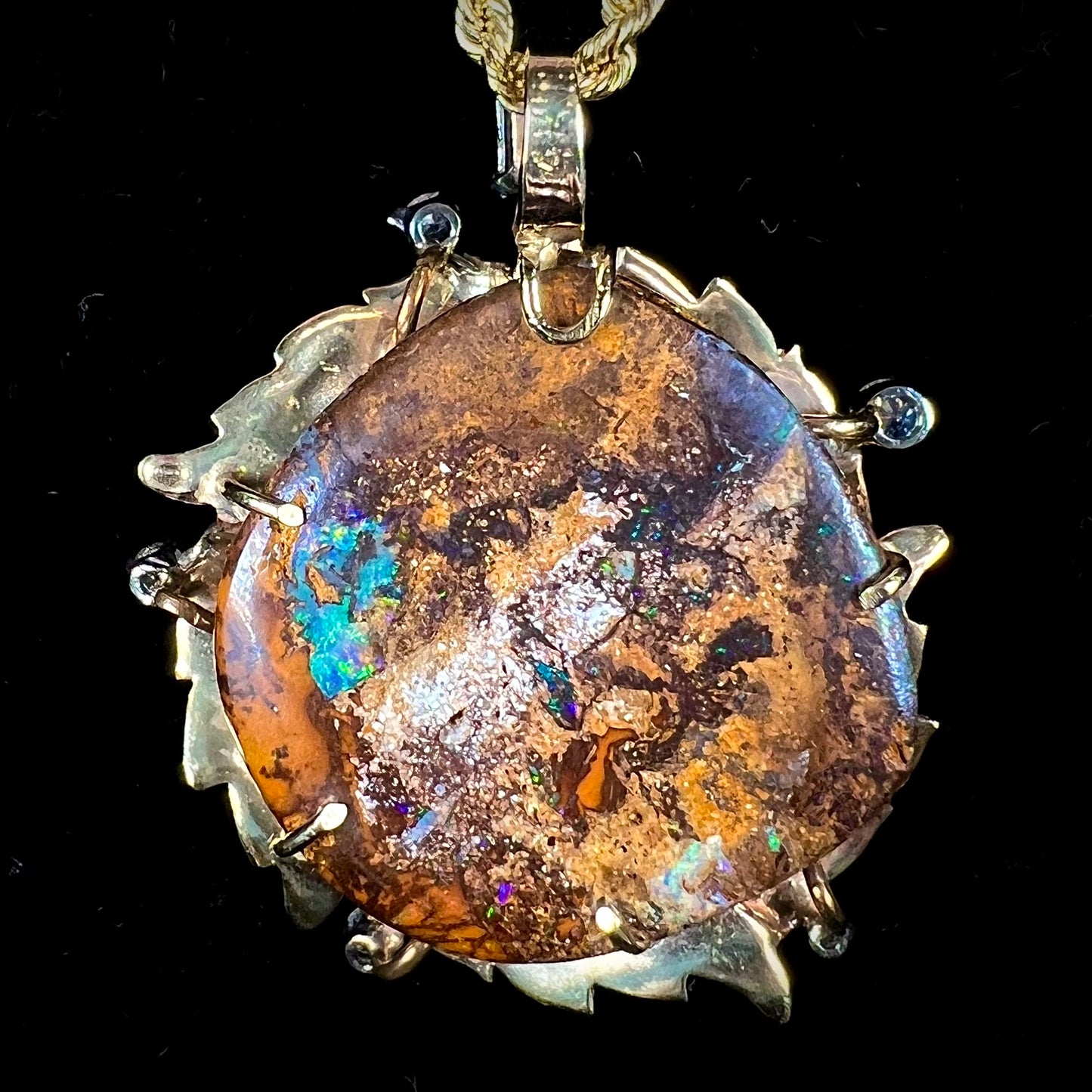 A gold opalized wood, diamond, and emerald pendant. The opal is set in a wreath of gold feathers that form a star.